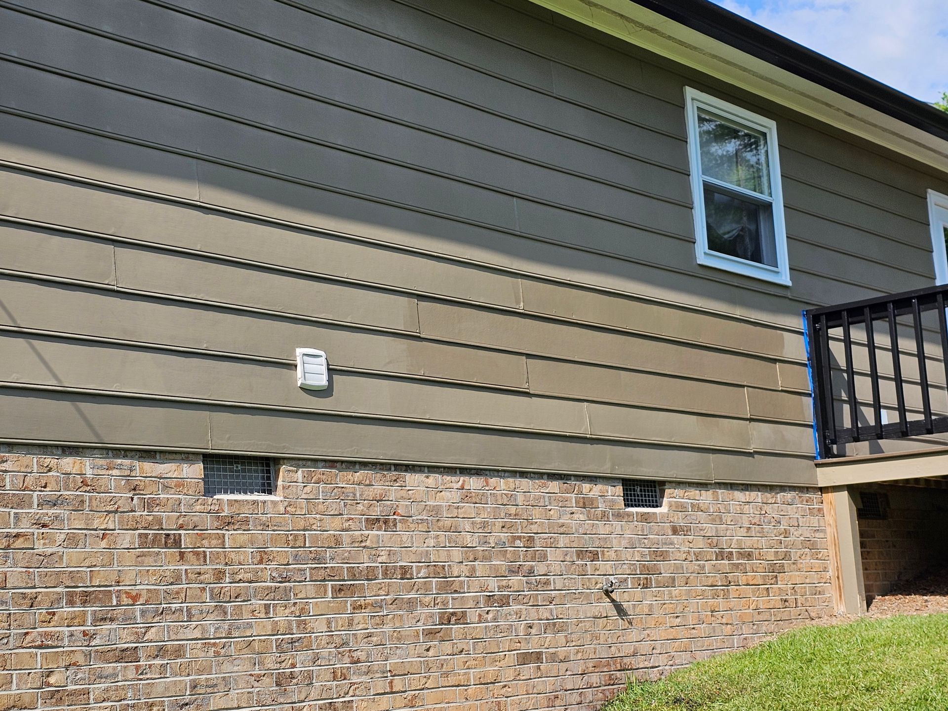 Brown house siding and brick foundation with a window and a deck.
