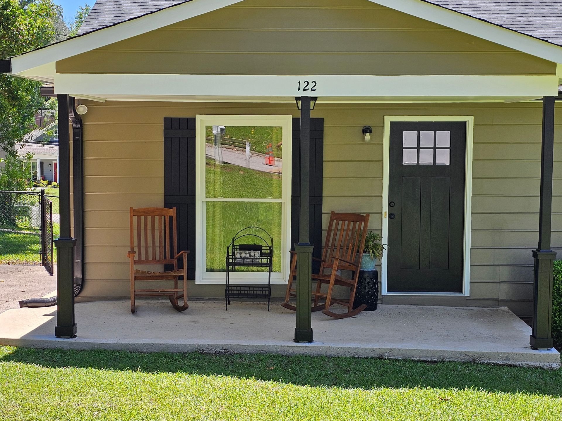 Small house porch with two rocking chairs, black door, and a large window.