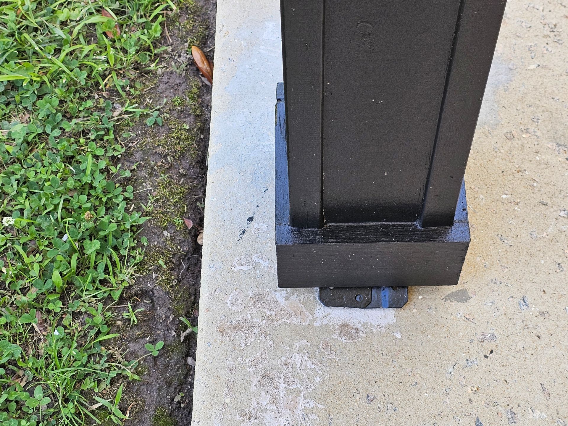 Black square post on a concrete surface next to grass.