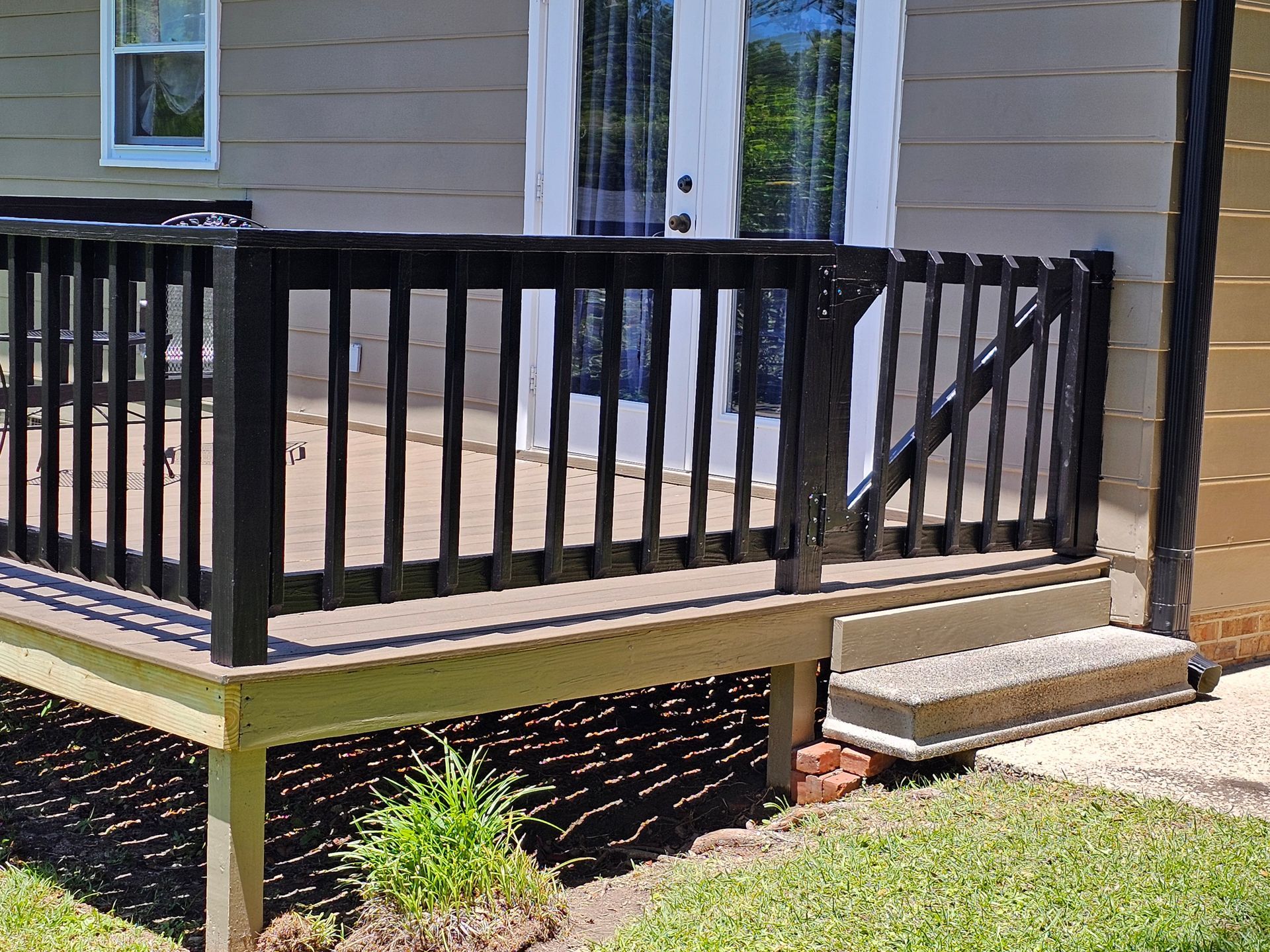 Deck with black railing, steps, and door. The deck is on a grassy lawn.