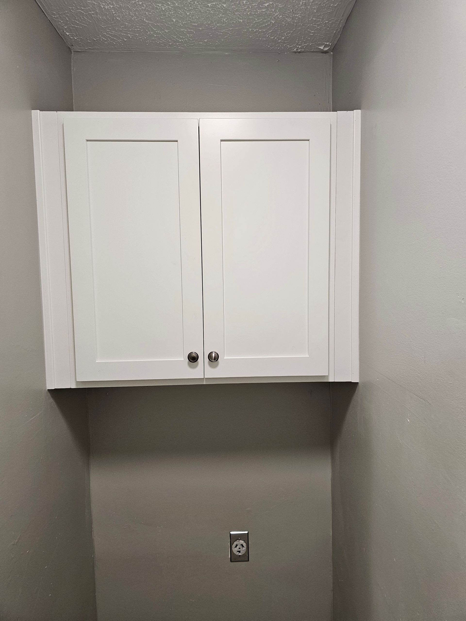 White cabinet mounted on a gray wall above an electrical outlet.