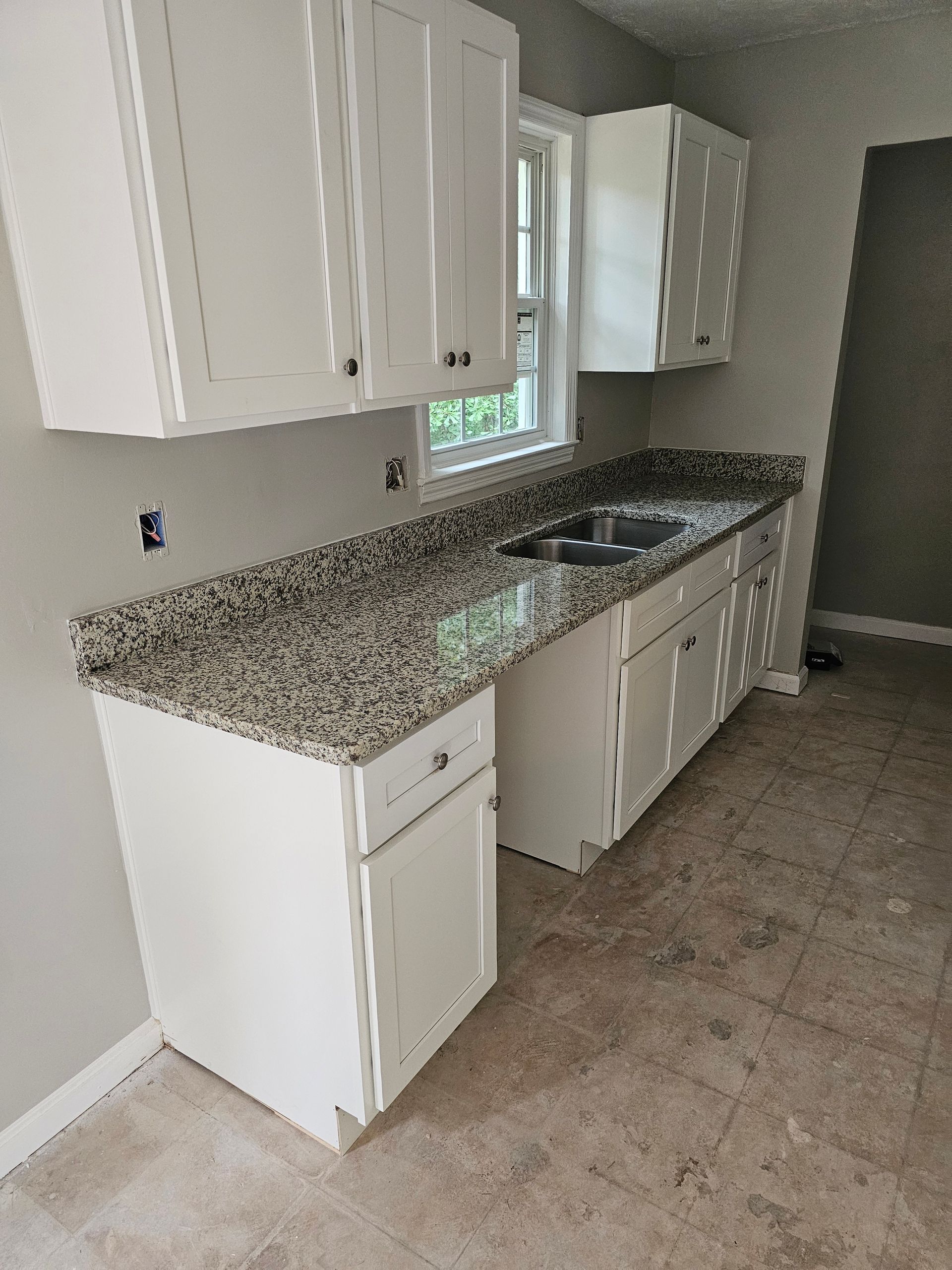 White kitchen cabinets and granite countertop in a room with a window, sink, and neutral flooring.