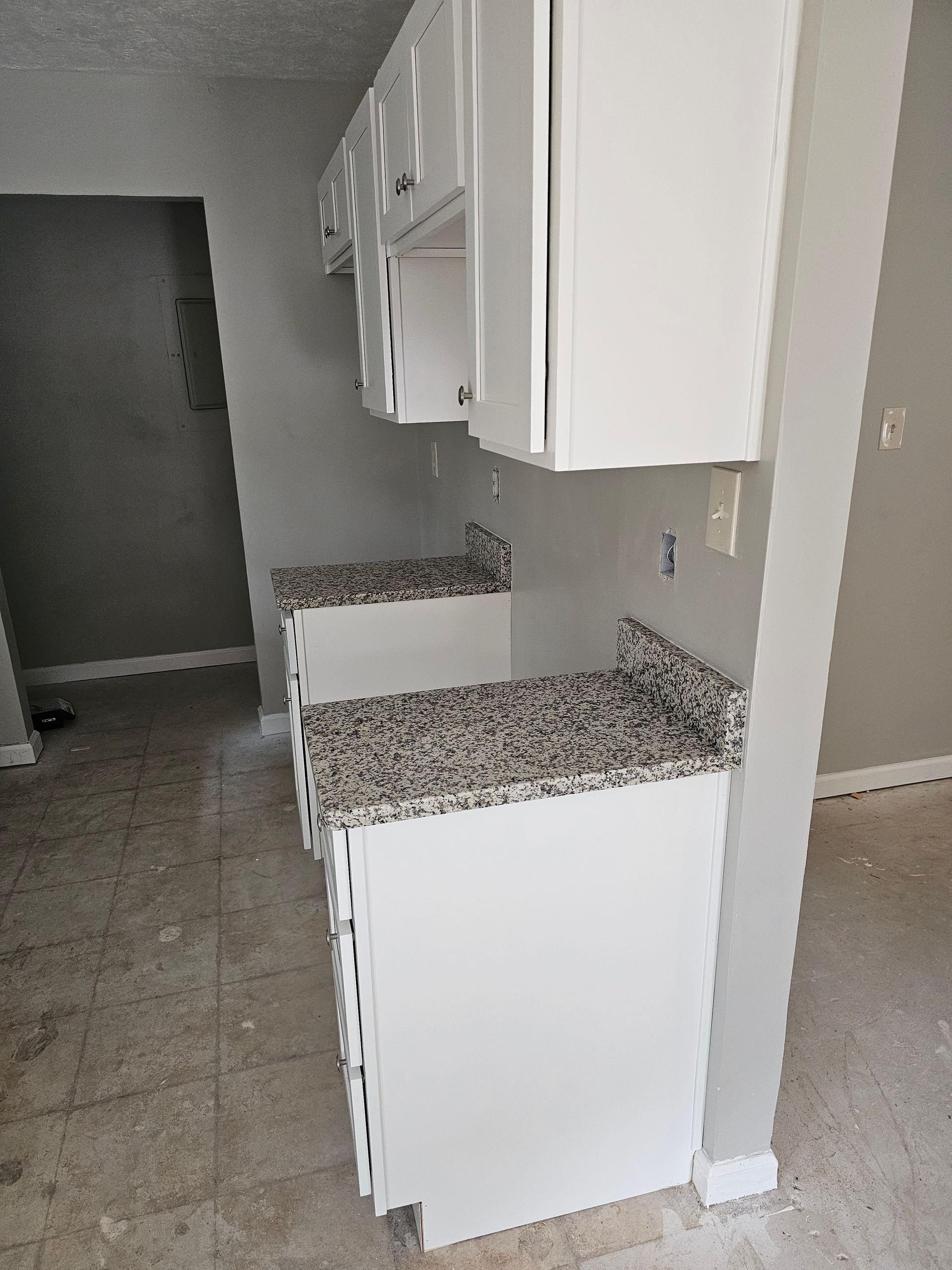 White kitchen cabinets with granite countertops. Gray walls and tile floor.
