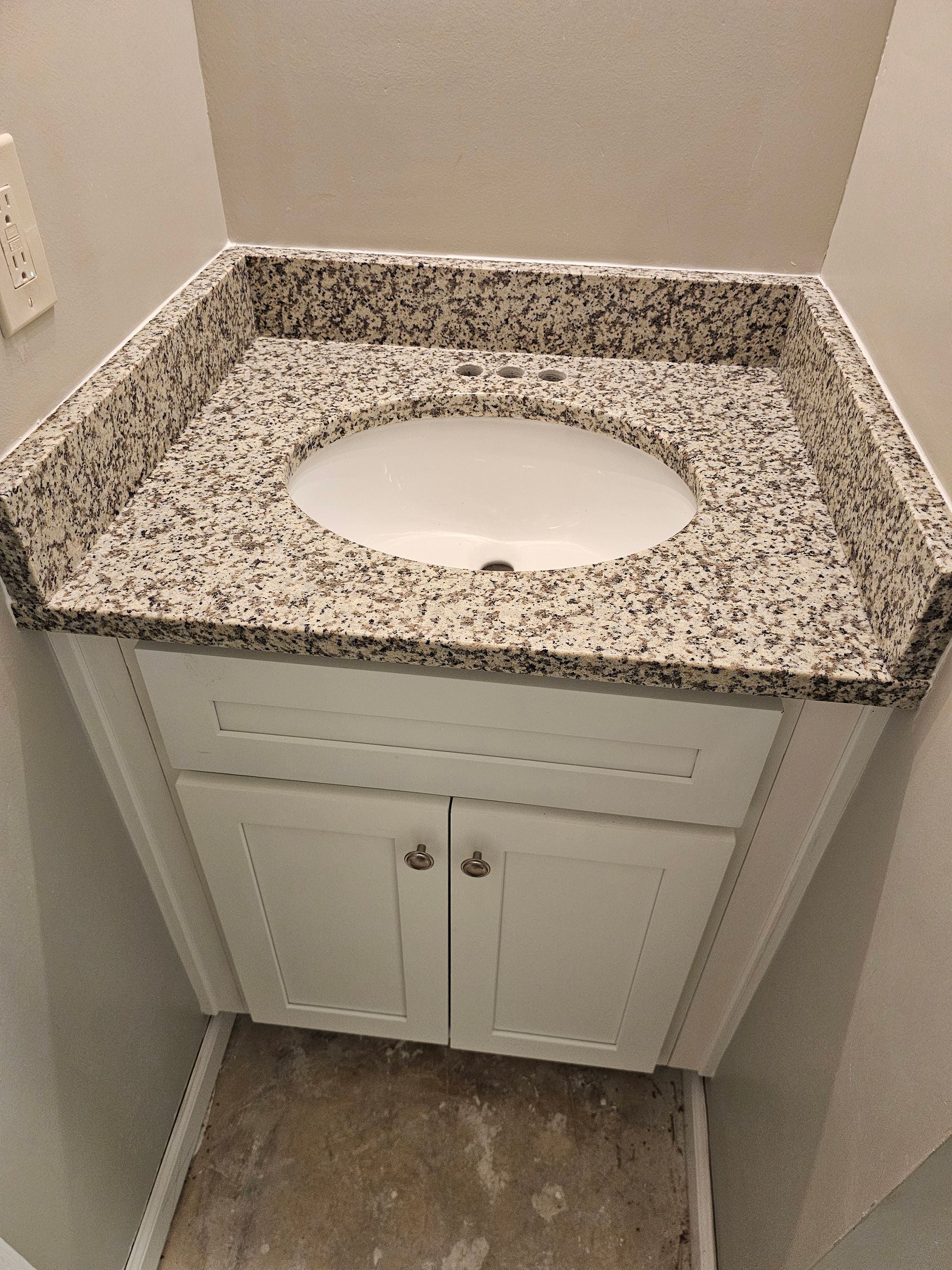 Bathroom vanity with a granite countertop and oval sink, set in a white cabinet.