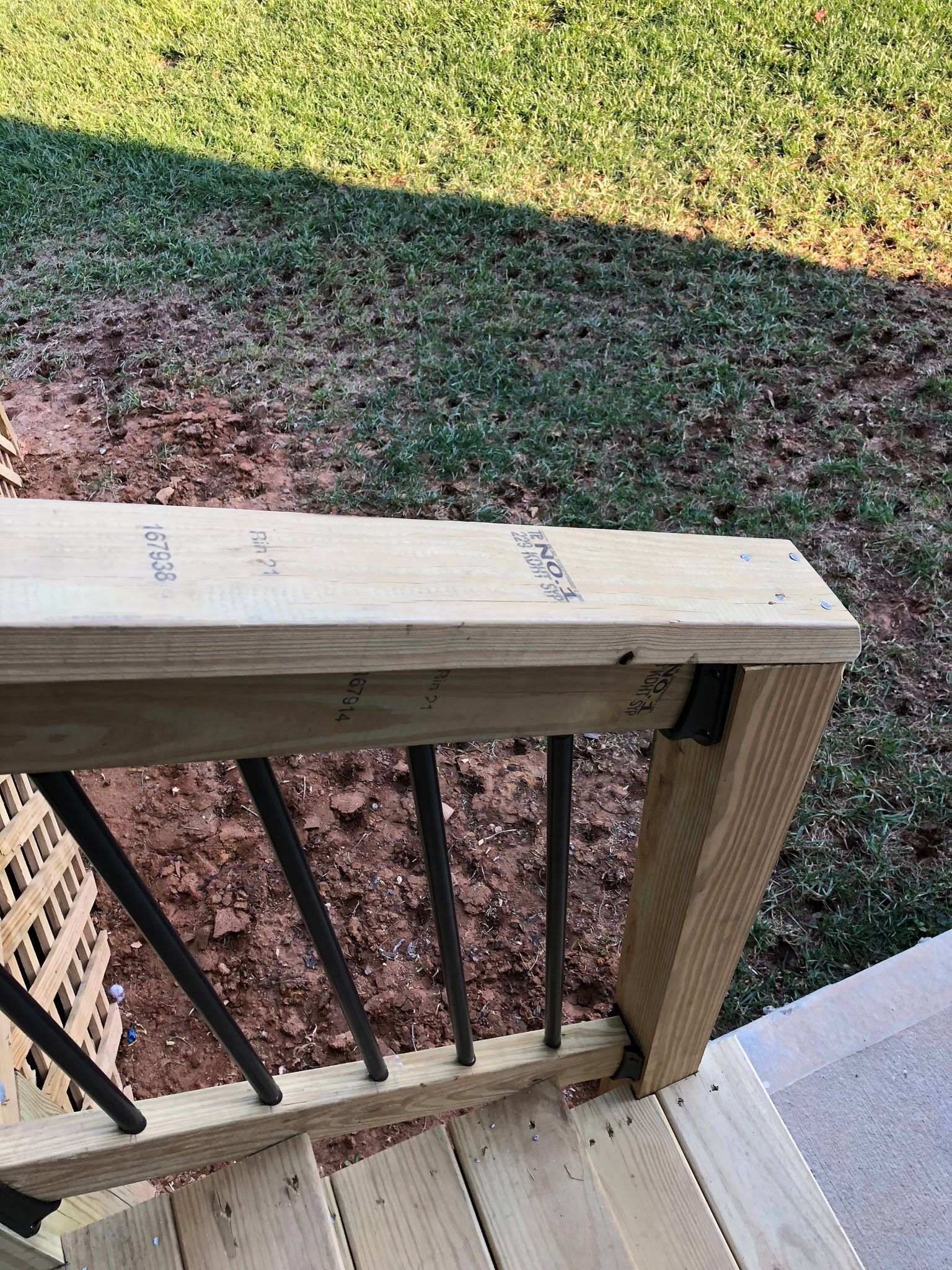 Wooden deck railing with black vertical spindles, and the yard in the background.