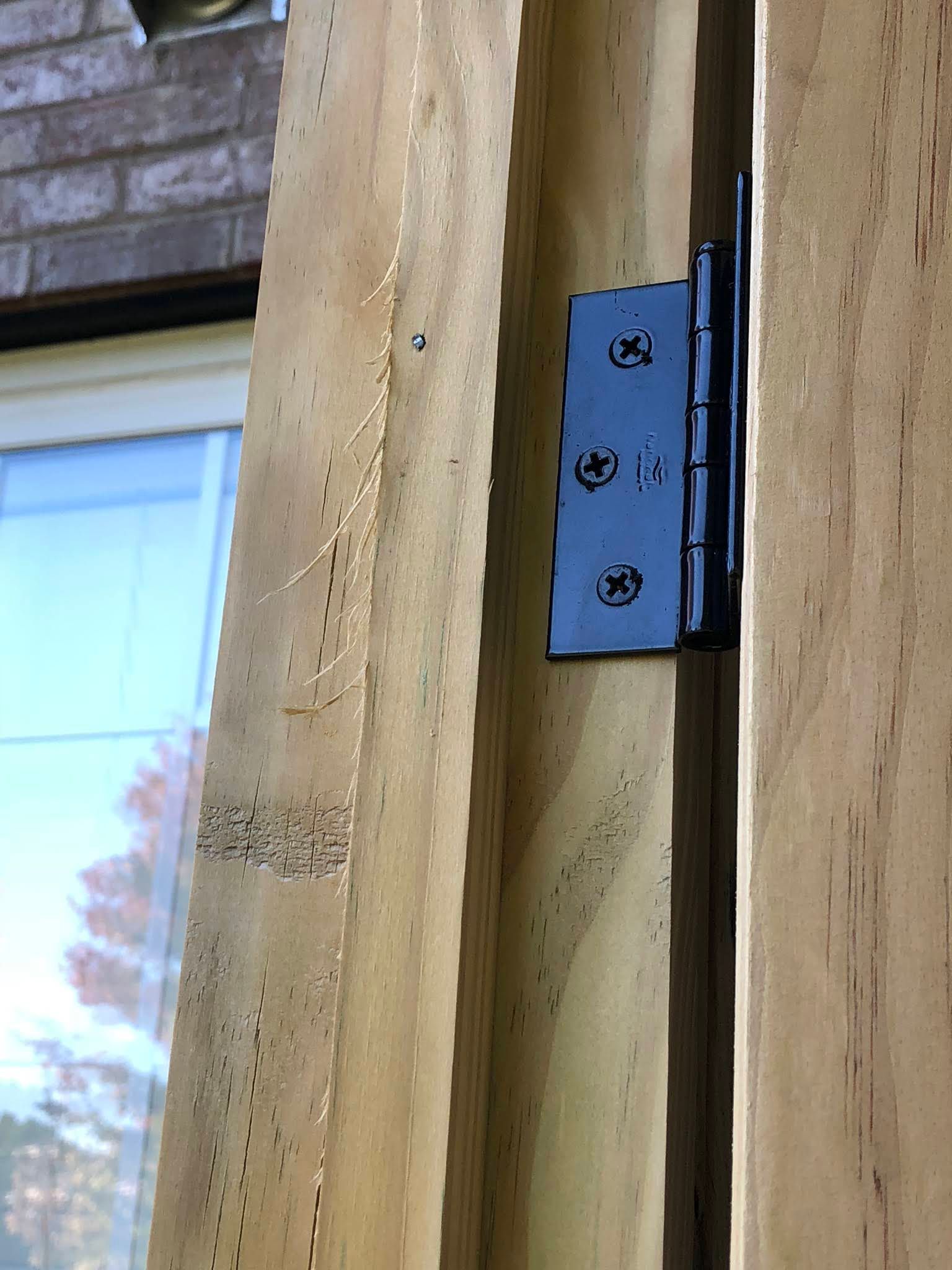 Black hinge attached to vertical wooden planks near a window and brick building.