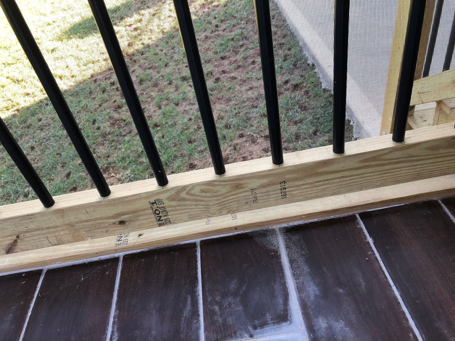 Close-up of black railing posts on a wooden deck, with screen mesh visible behind them.
