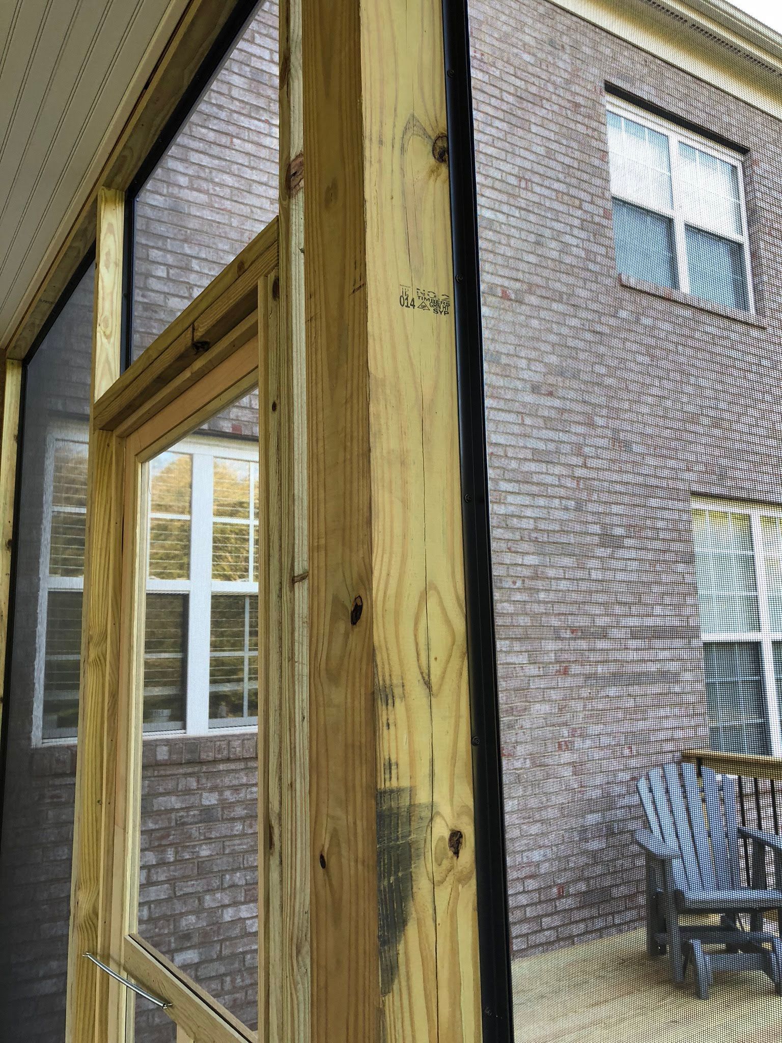 Wooden porch framing with a window and brick building visible through the screen.