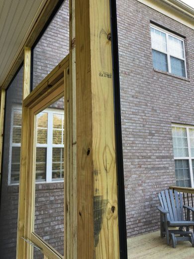 Wooden frame of a screened porch, with a view of a brick house through a window.