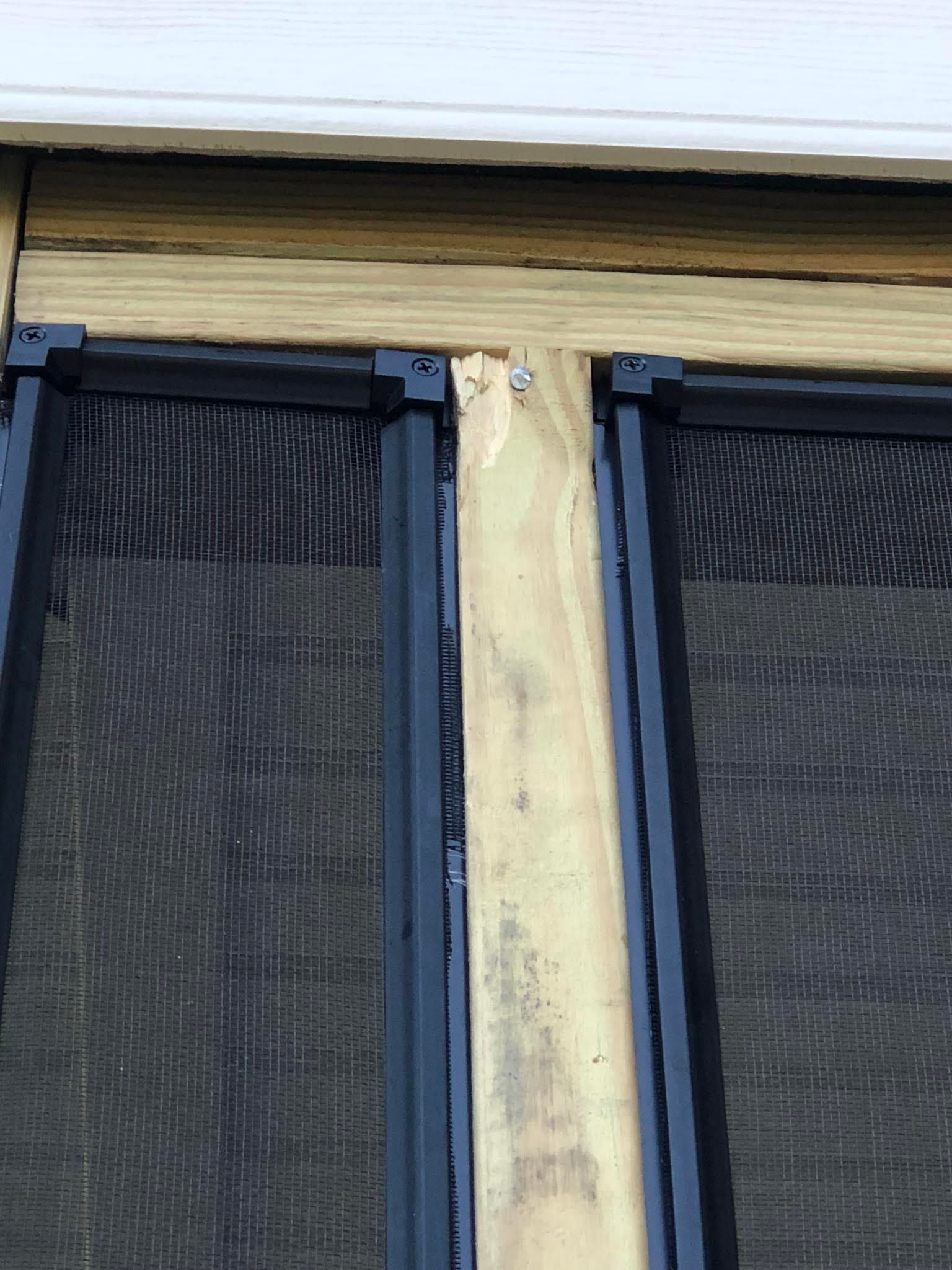 Two black screen doors and wood frame against a white wall.