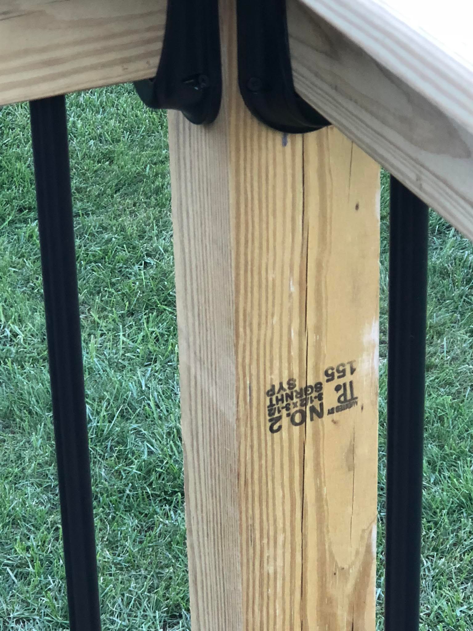 Wooden deck post with attached black metal railing supports. Green lawn in the background.