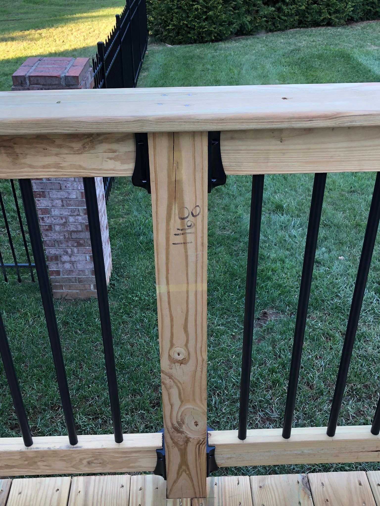 Wooden deck railing with black metal spindles and a grassy background.