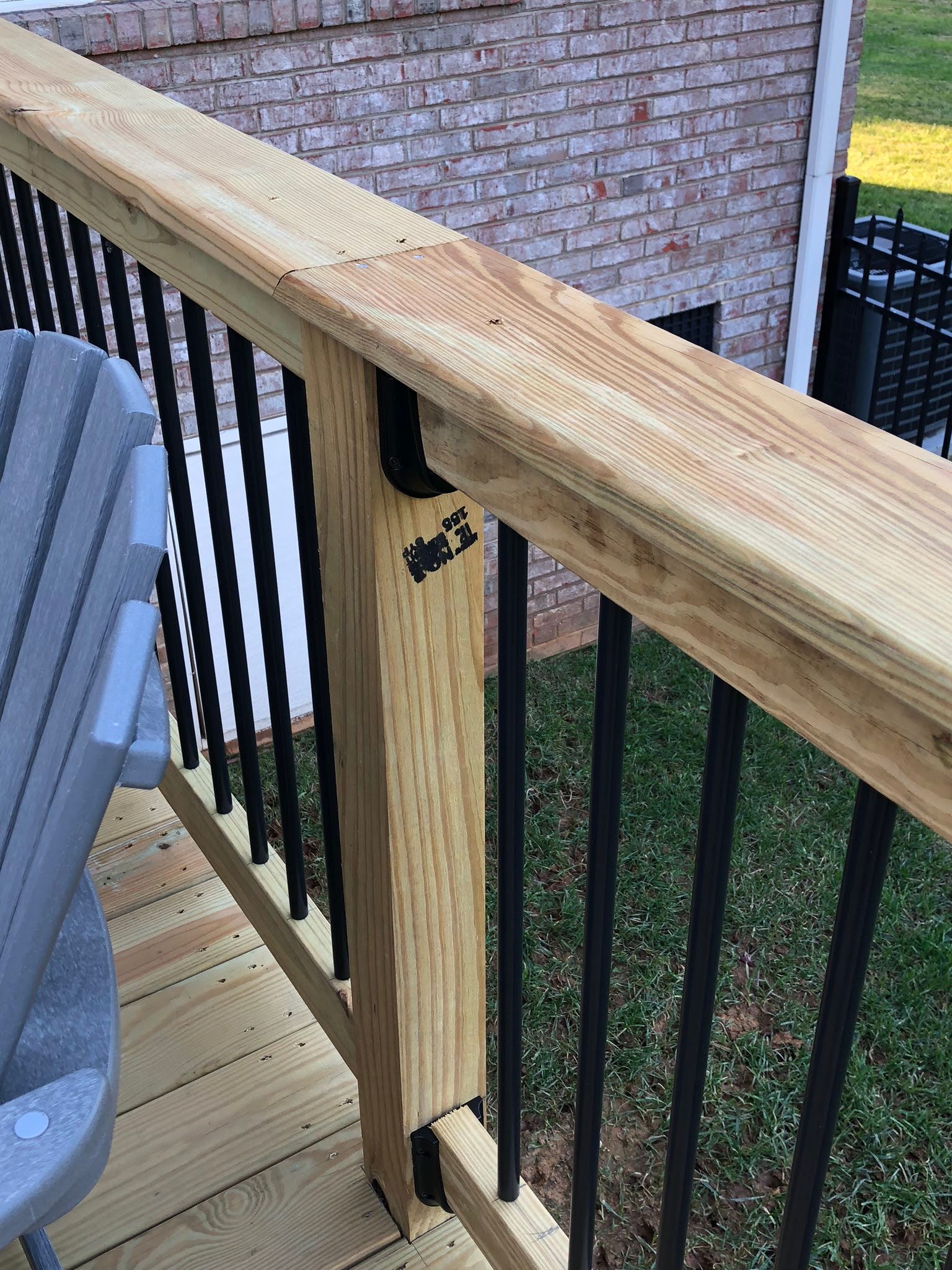 Wooden deck railing with black vertical spindles, set against a brick wall.