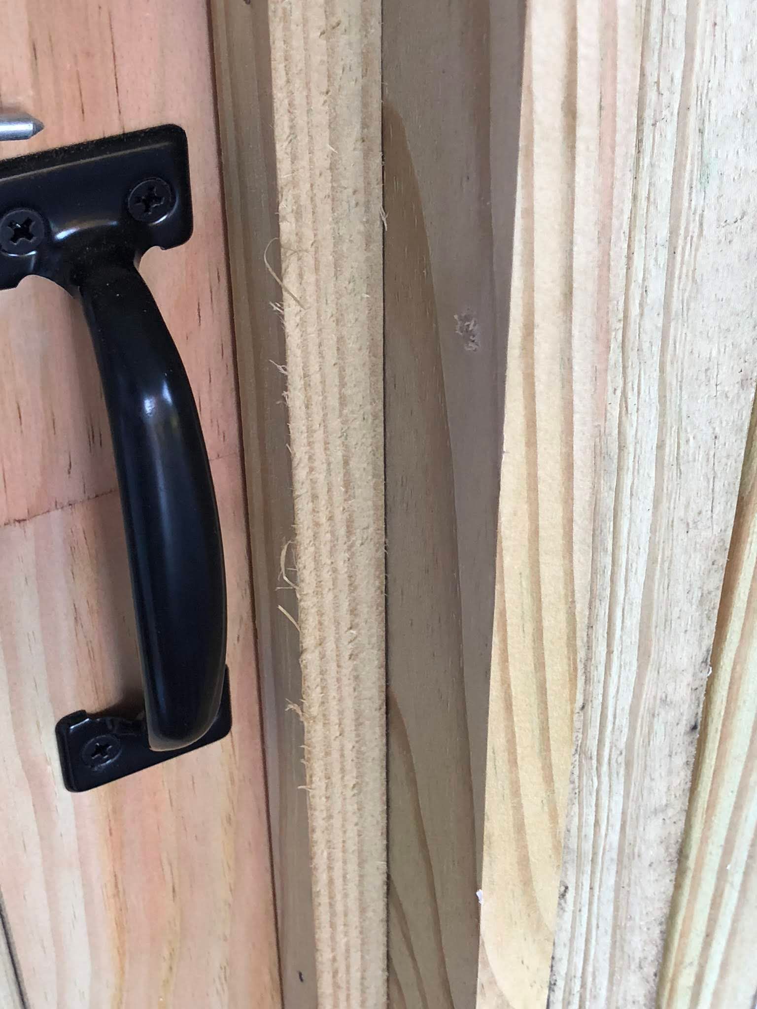 Black handle attached to a wooden surface, with a thin wooden plank next to it.