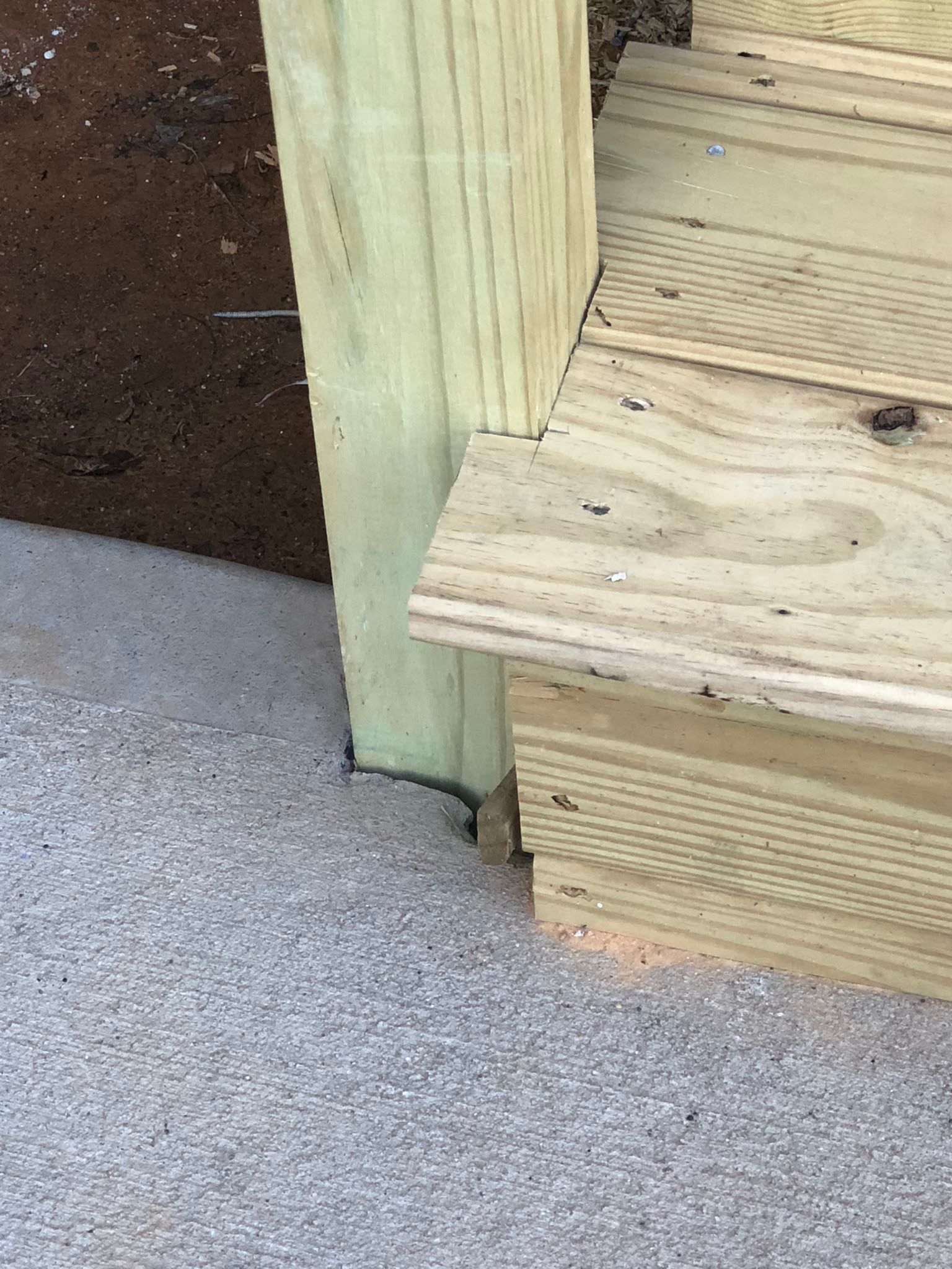 Wooden deck steps with a post on gravel.