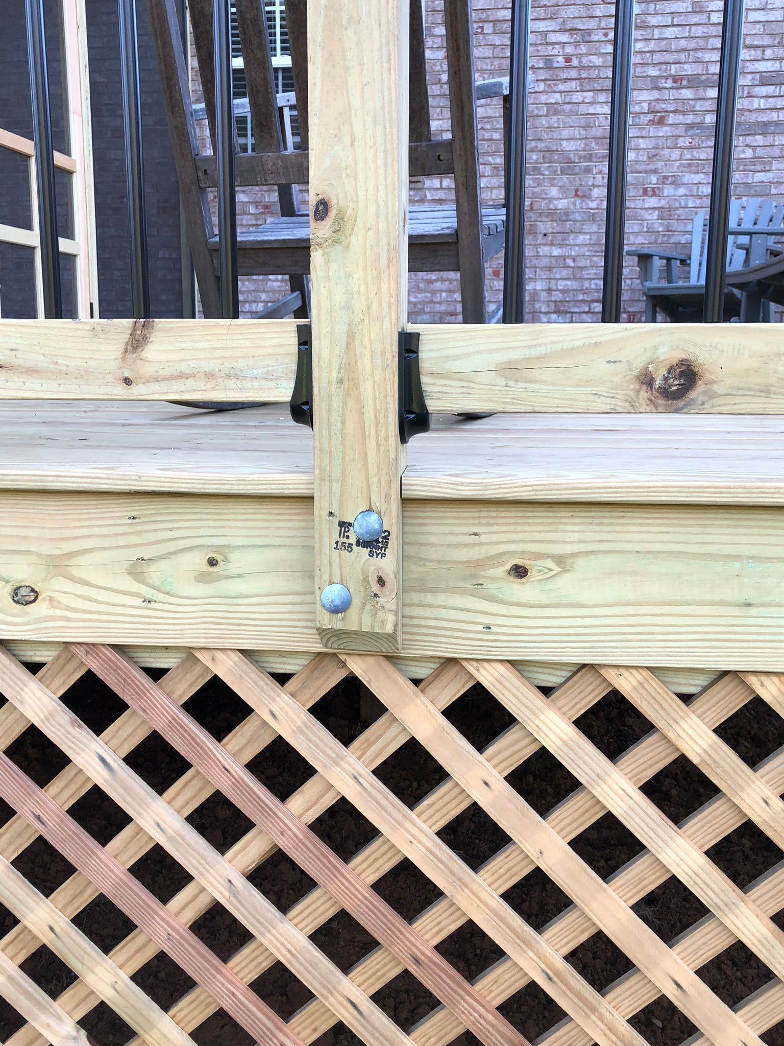 Wooden deck with lattice and railing post, secured with black brackets.