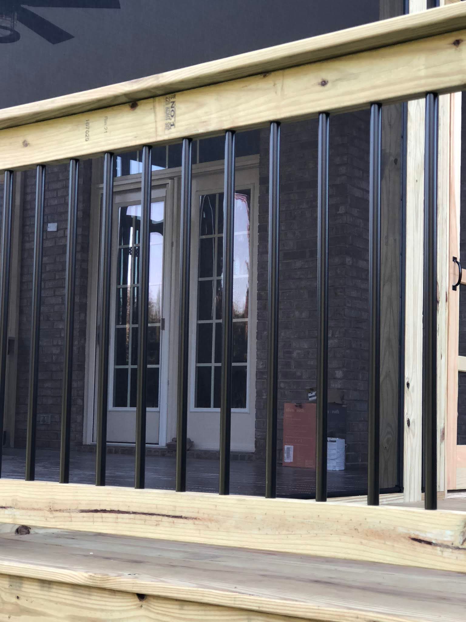 Wooden deck railing with black twisted metal balusters, and a brick wall.