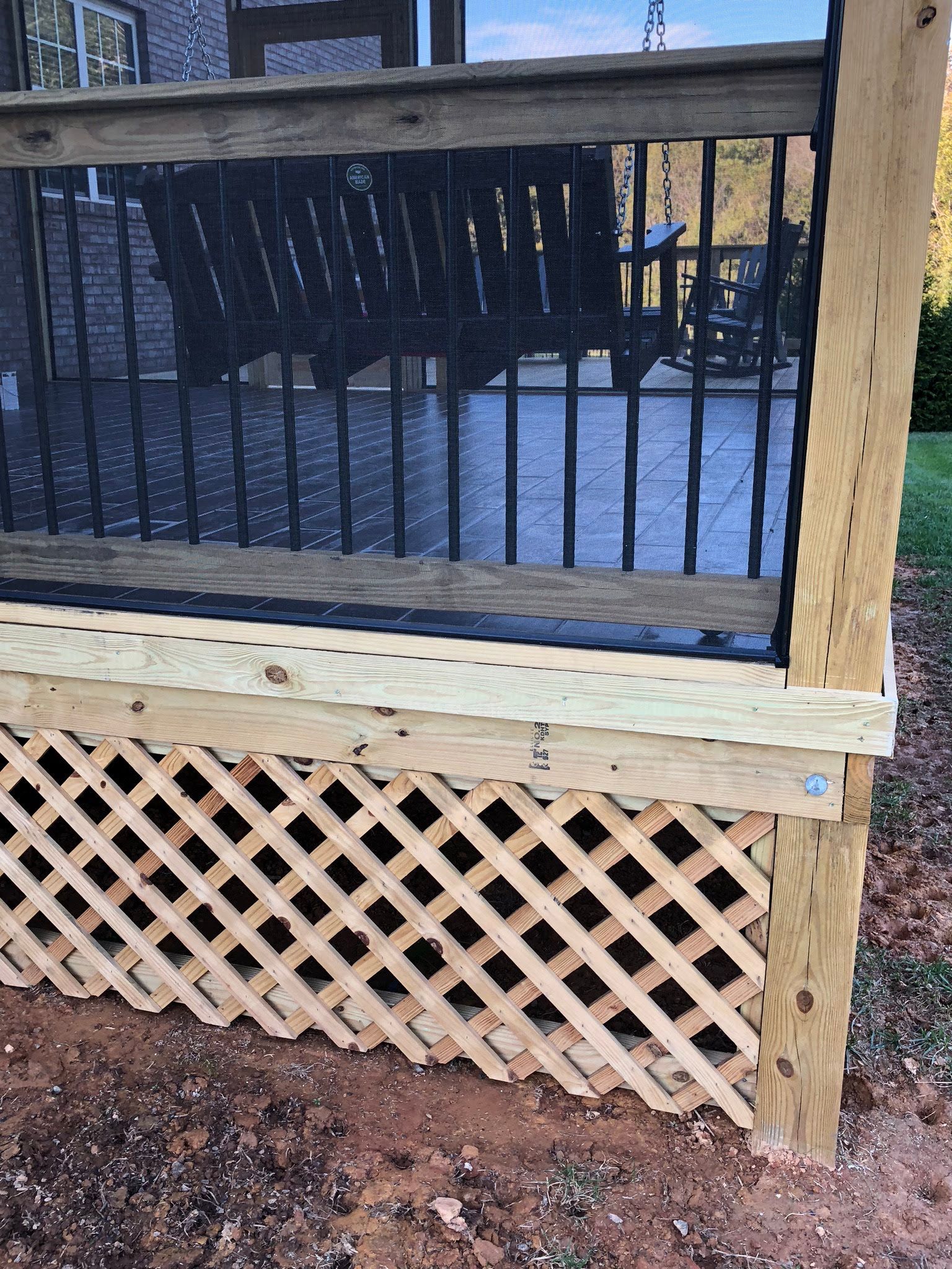 Lattice skirting on a deck with a black mesh screen, a swing, and a wooden railing post.