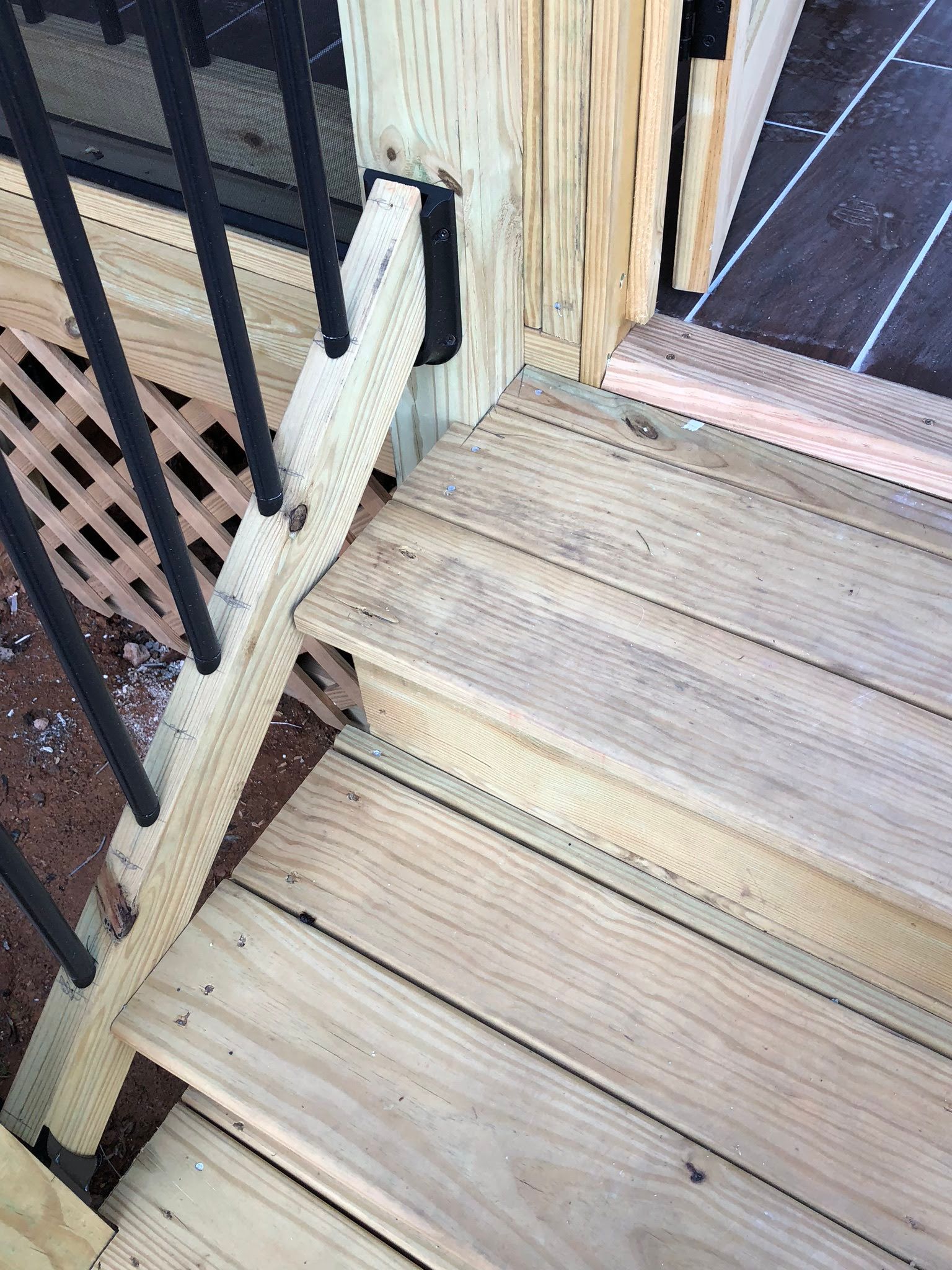 Wooden deck stairs with black railing and lattice.