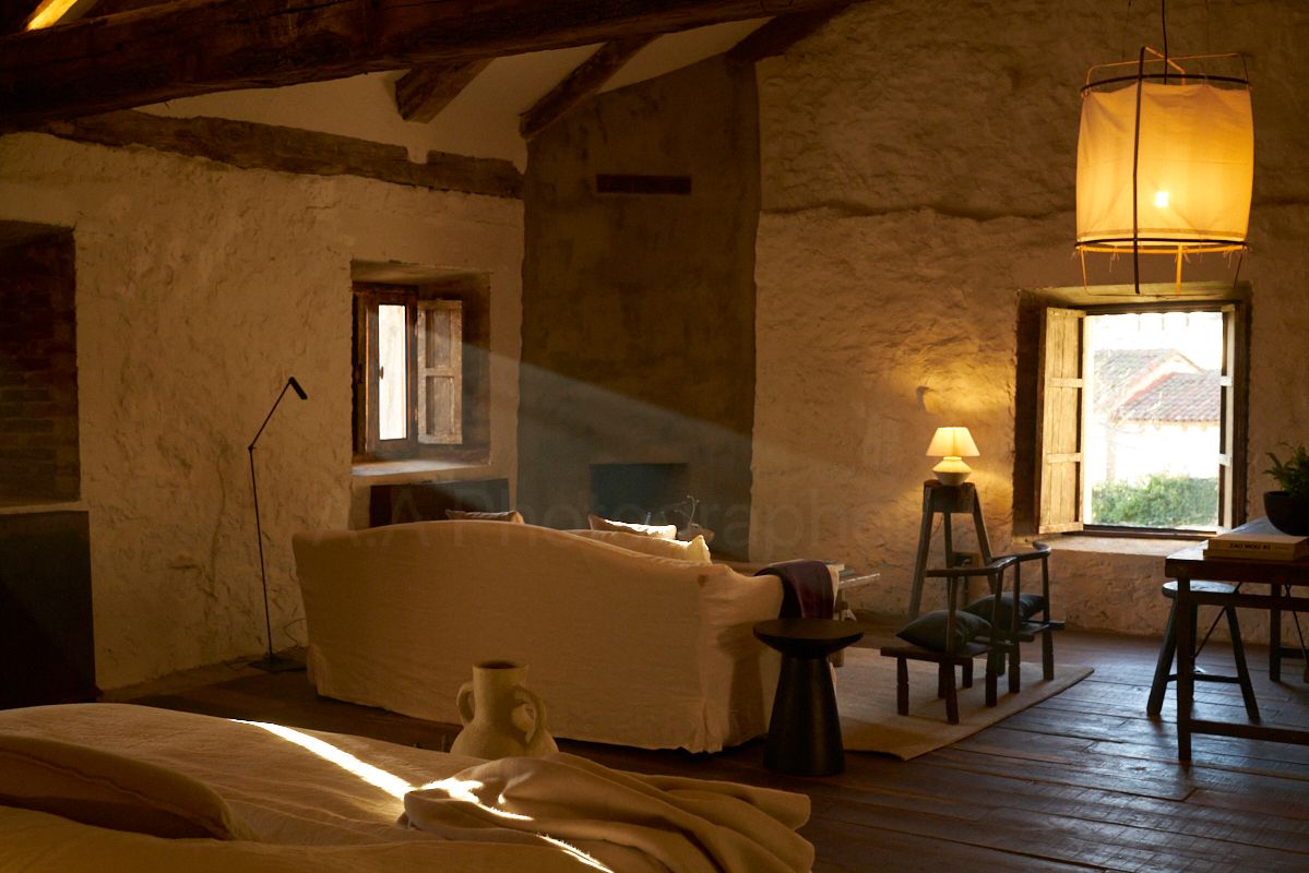 Living room of apartment 7 lit by a halo of natural light. Whitewashed stone, concrete fireplace, and wabi sabi antiques.