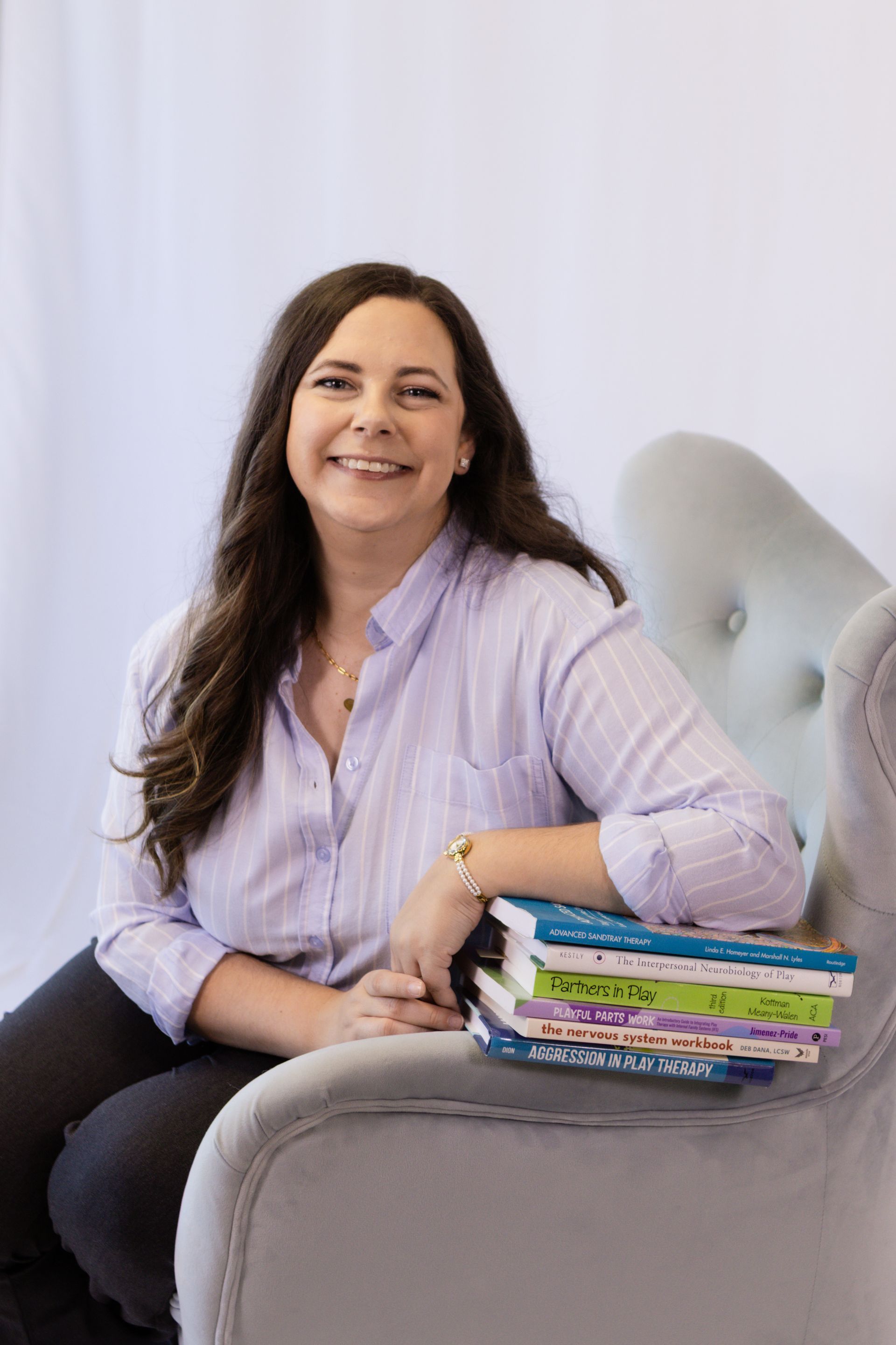 a woman sitting in a blue chair with books . Megan Cinnamon, LPCC-S