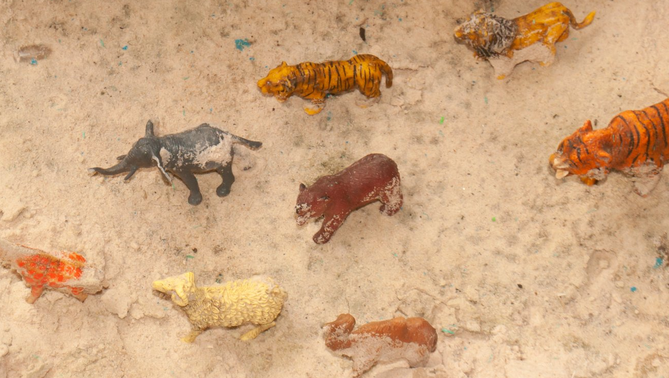 A group of plastic animals are standing in the sand.
