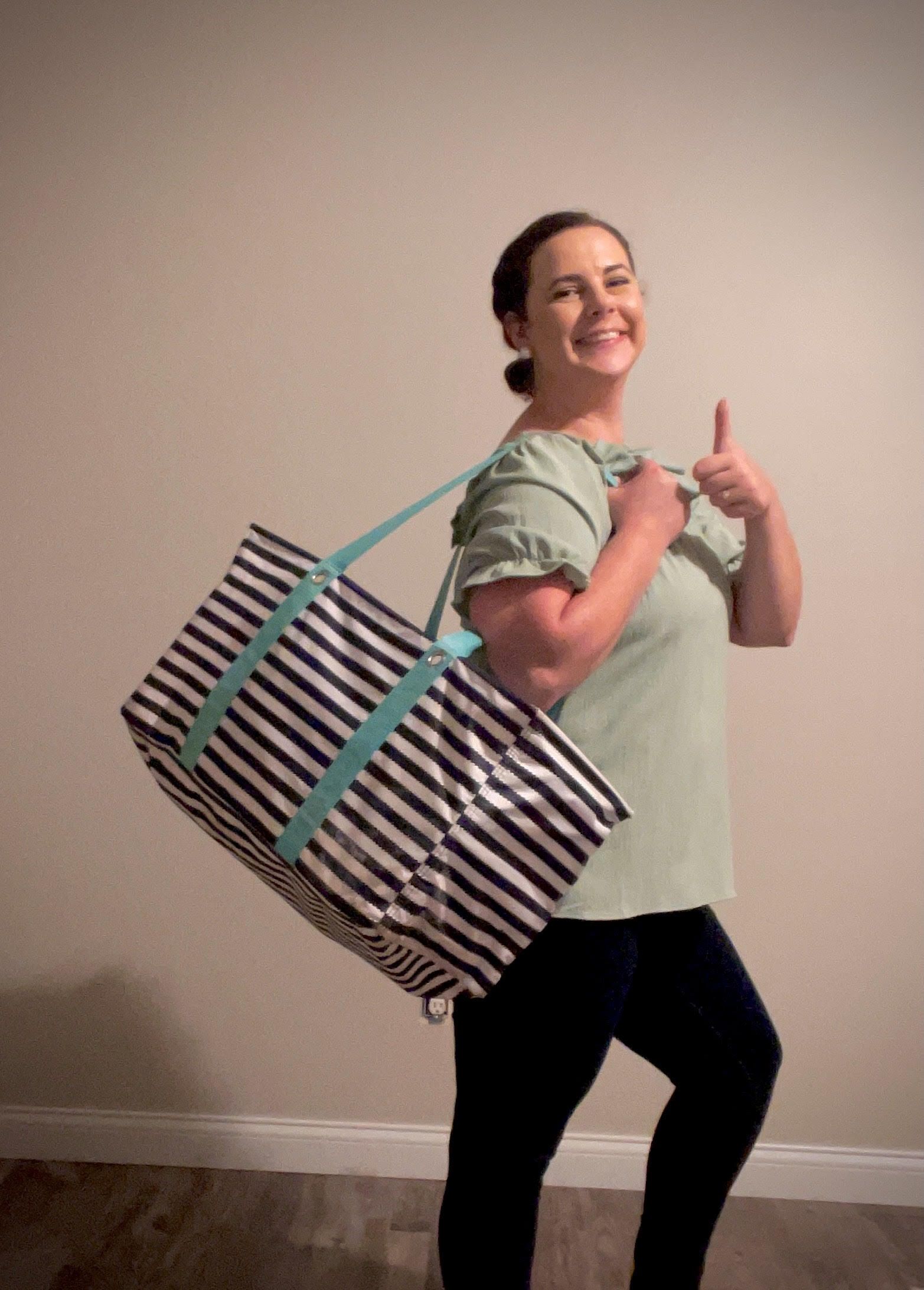 A woman is holding a striped tote bag and giving a thumbs up.