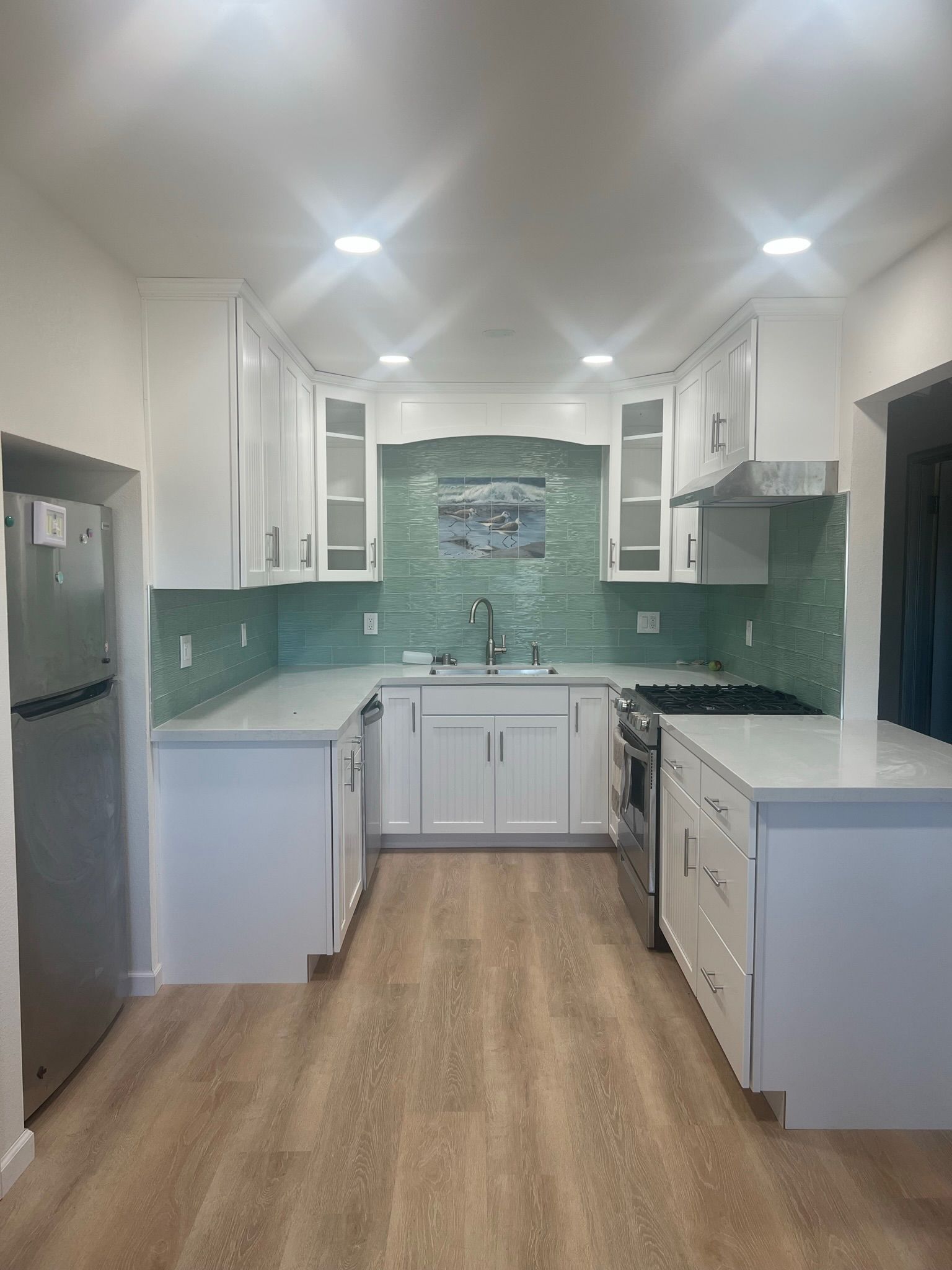 Bright, white kitchen with pale blue backsplash and light wood-look flooring. Stainless steel appliances.