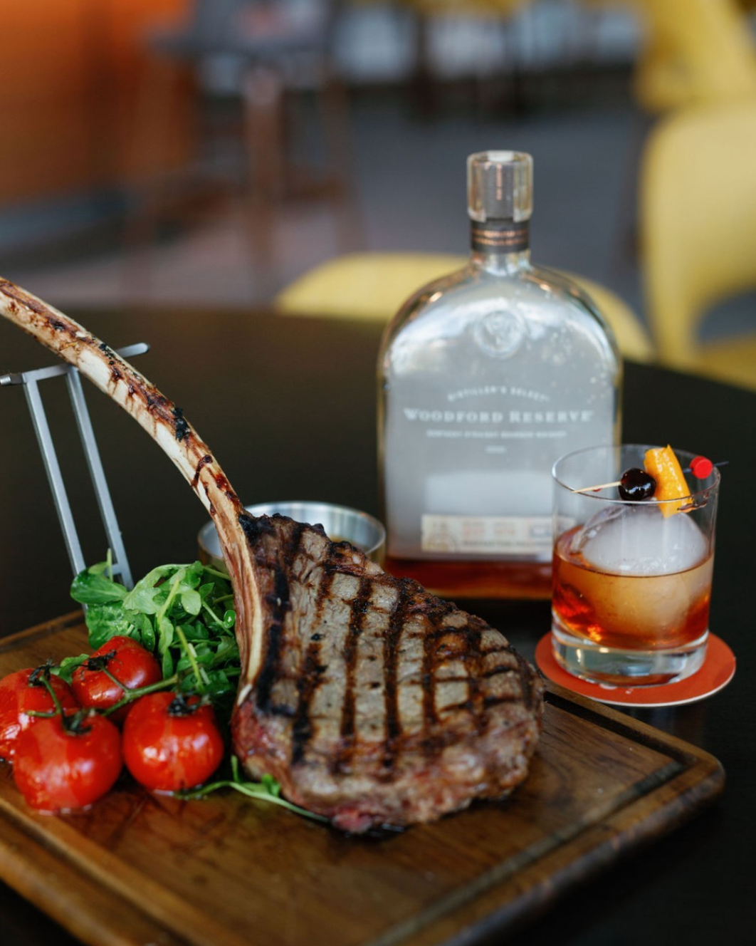 Rack of lamb and tomatoes on a platter. Accompanied by a fancy whiskey cocktail.