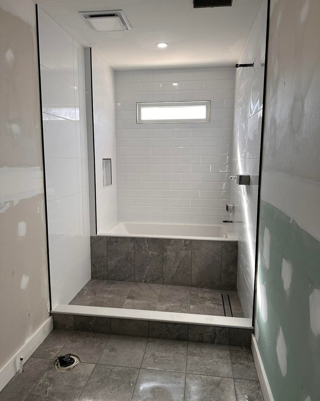 Bathroom under construction with gray tile floor and shower area, white and gray tiled walls, and a built-in tub.