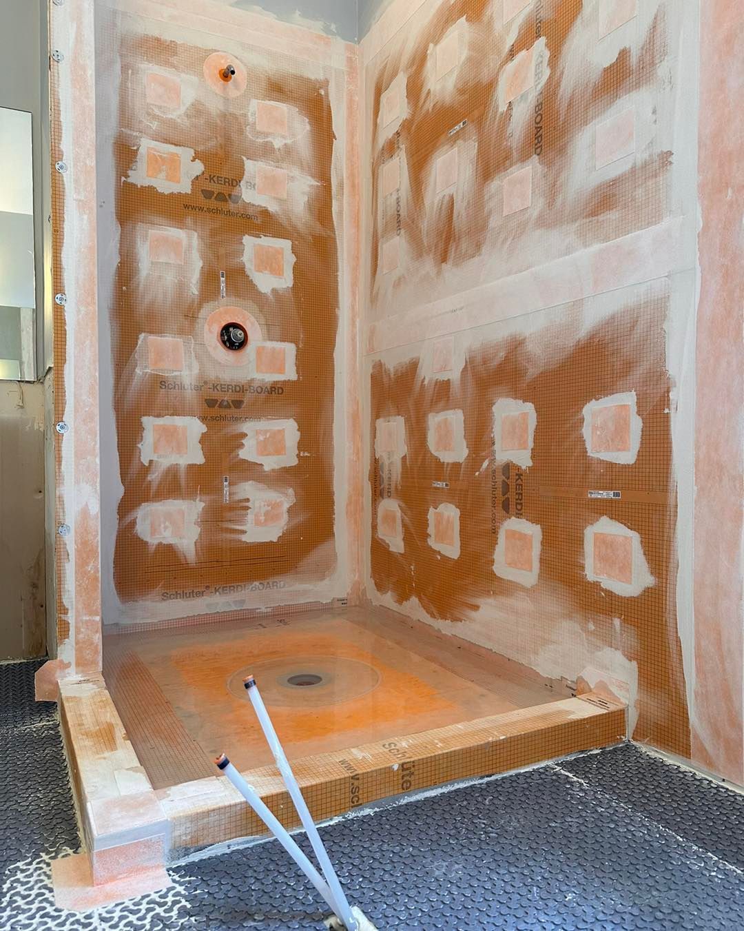 Shower stall under construction, orange panels, white sealant, drain in floor.