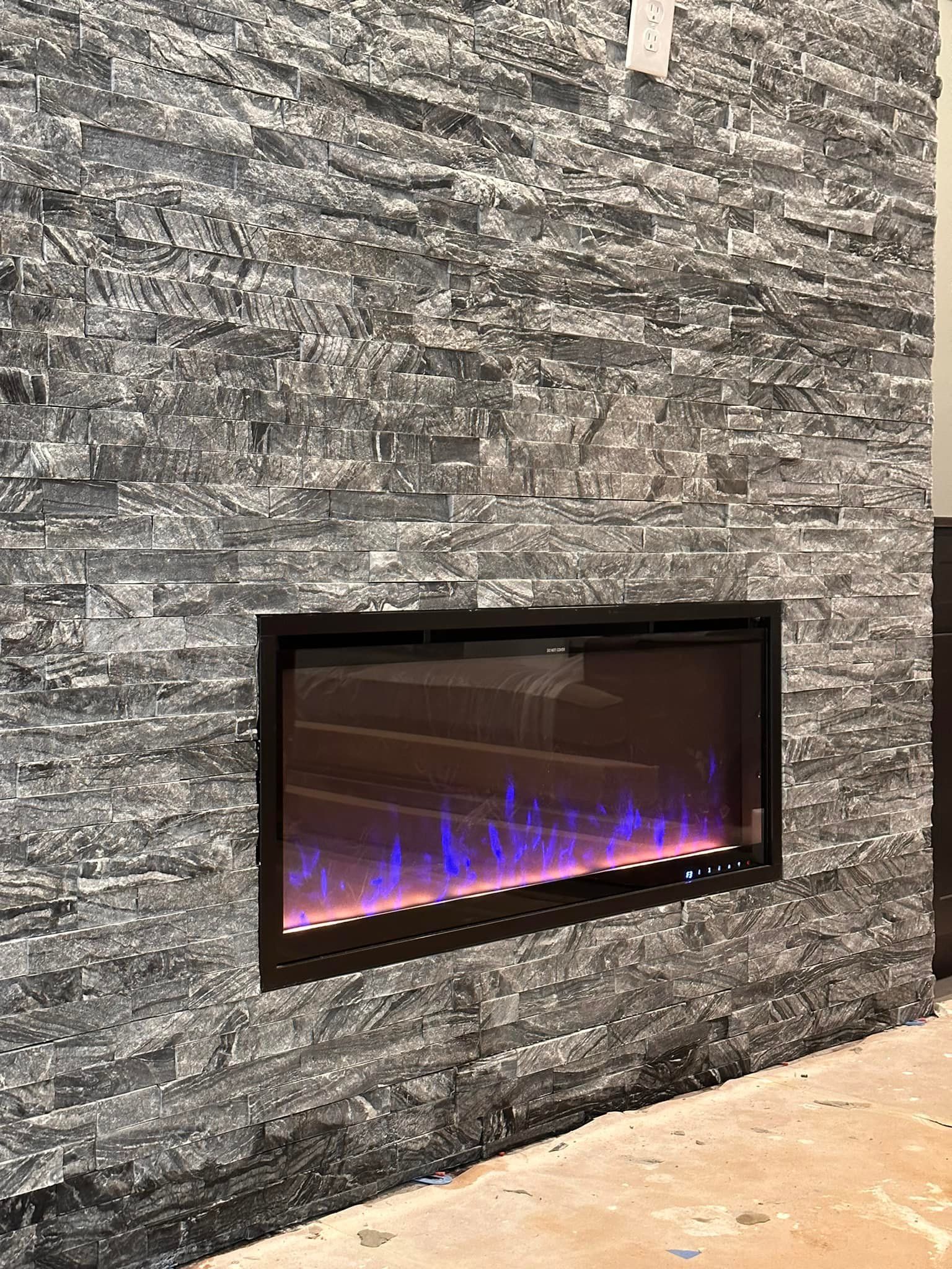 Electric fireplace with blue and orange flames set in a gray stone wall.