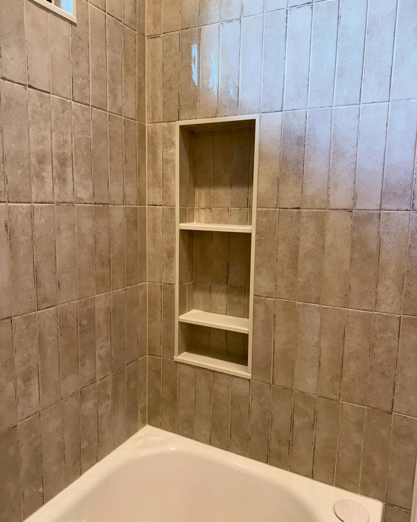 Tiled shower with built-in shelf; tan walls and white tub visible.