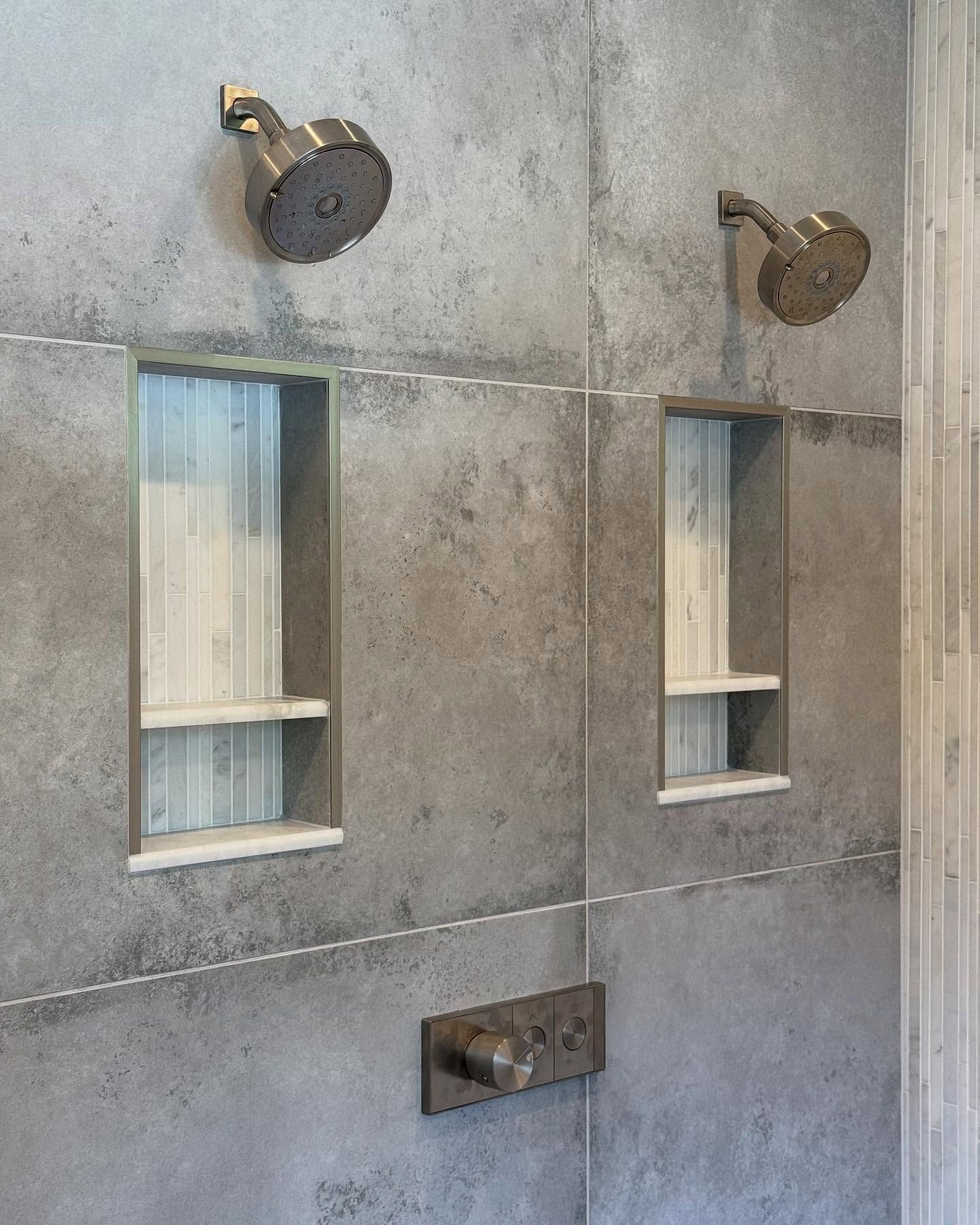 Gray tiled shower with two bronze showerheads, two inset shelves, and water controls.