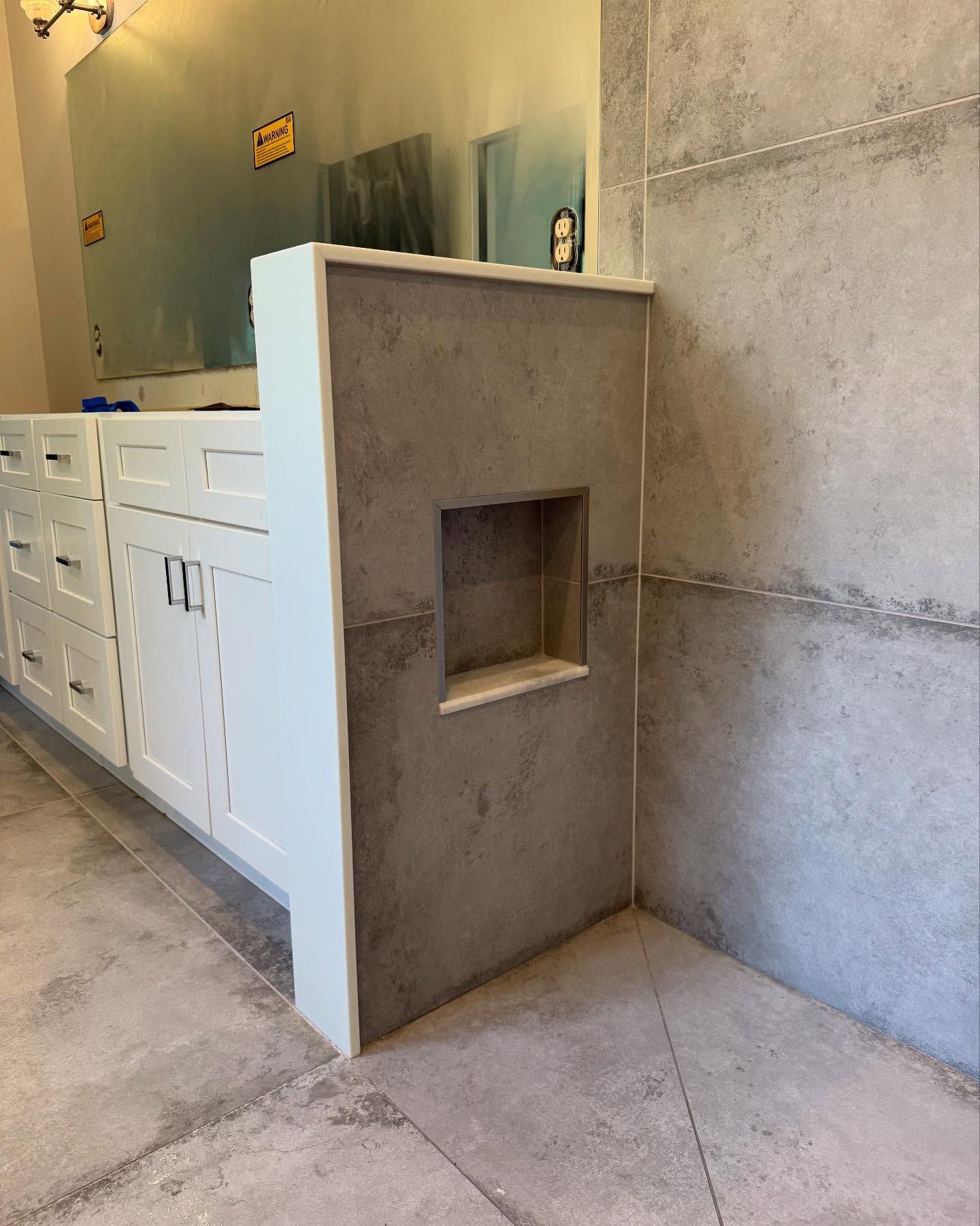Bathroom with white cabinets, gray concrete-style wall, and a small recessed shelf.