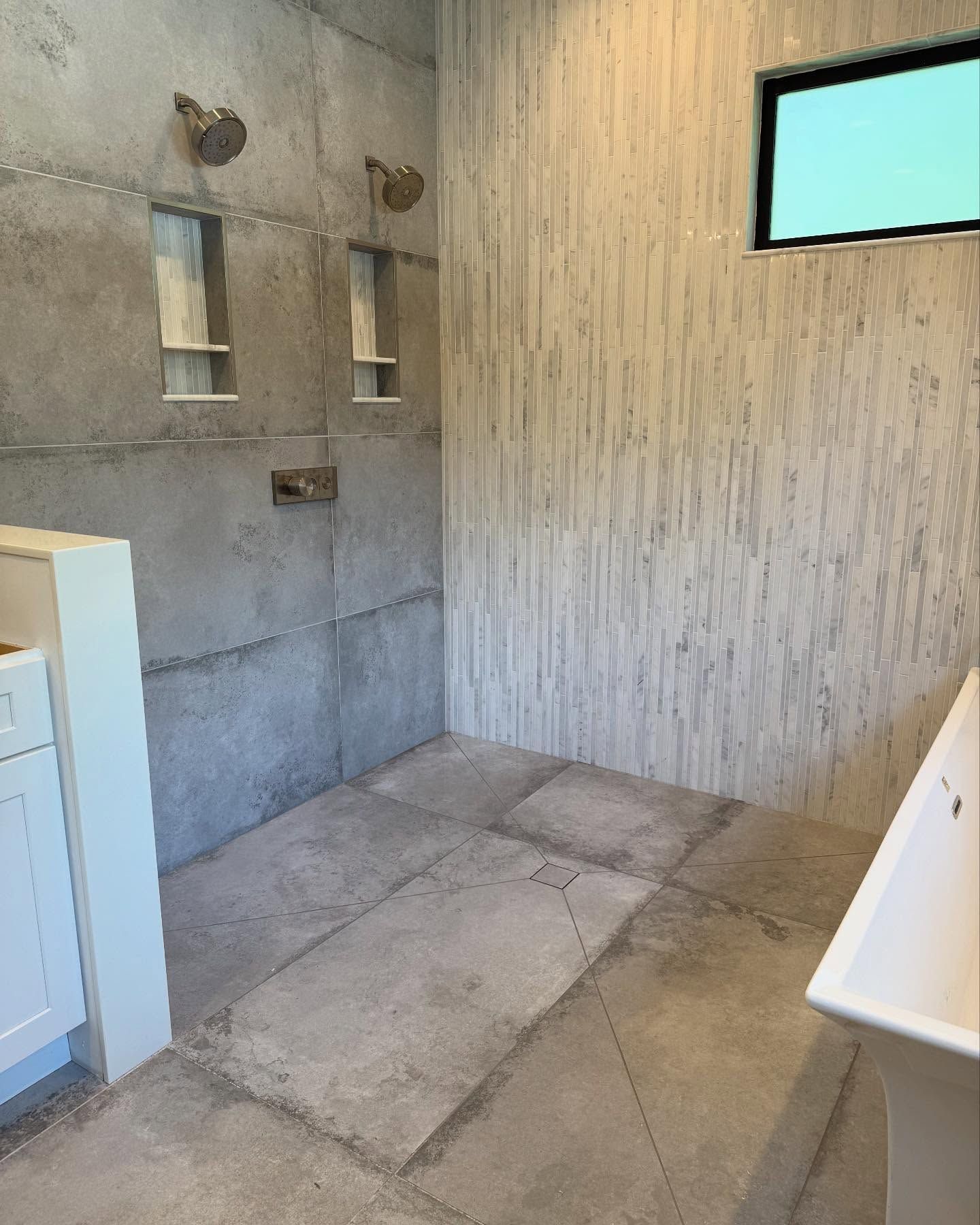 Concrete shower with two showerheads, recessed shelves, and a window. Grey and white tones.