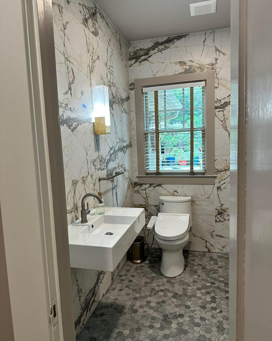Small bathroom with marble tile, white sink and toilet, and a window.
