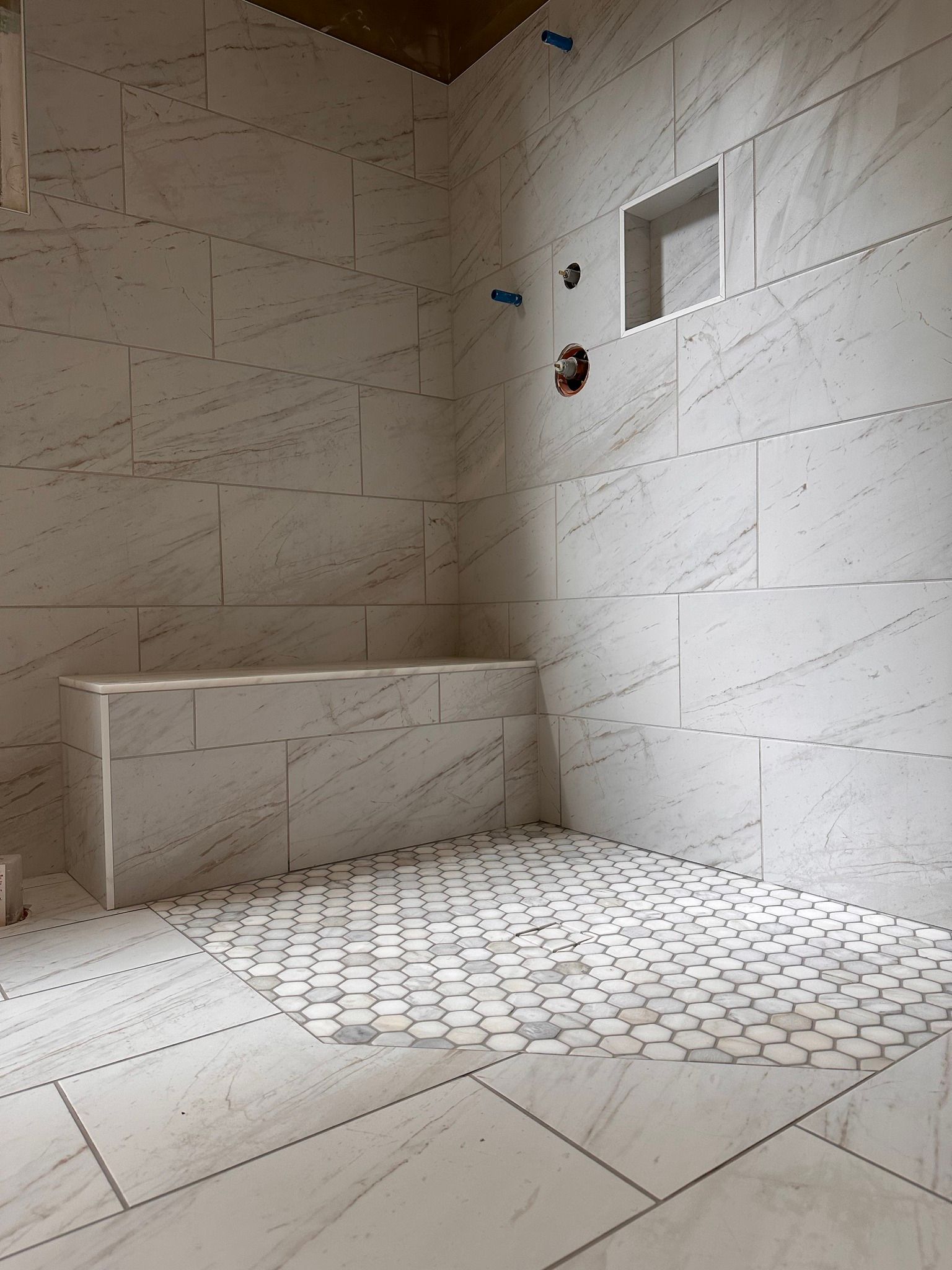 Bathroom with white tile walls and floor, a shower bench, and a recessed shelf.
