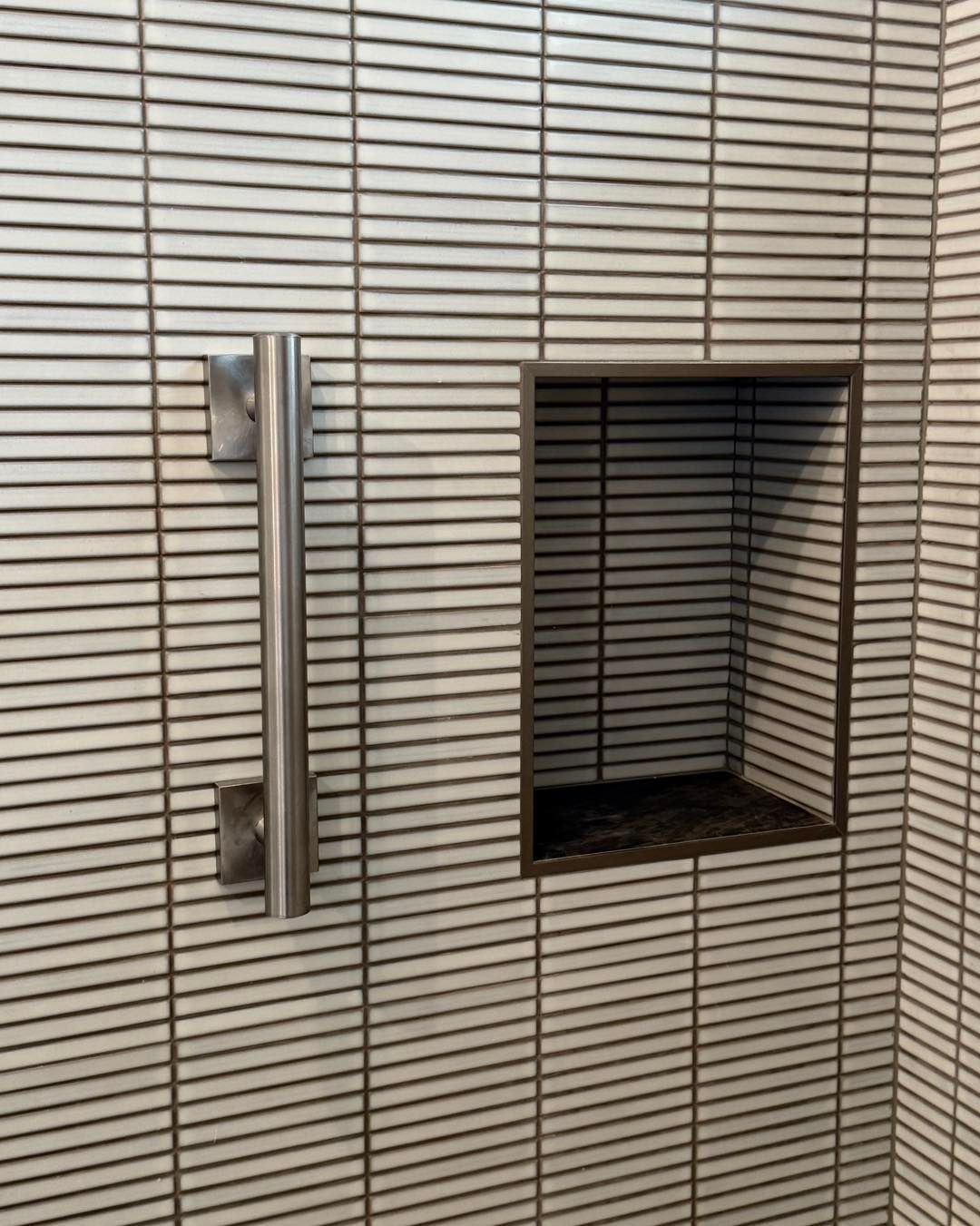 Shower with white horizontal tile, stainless steel grab bar, and a built-in shelf.