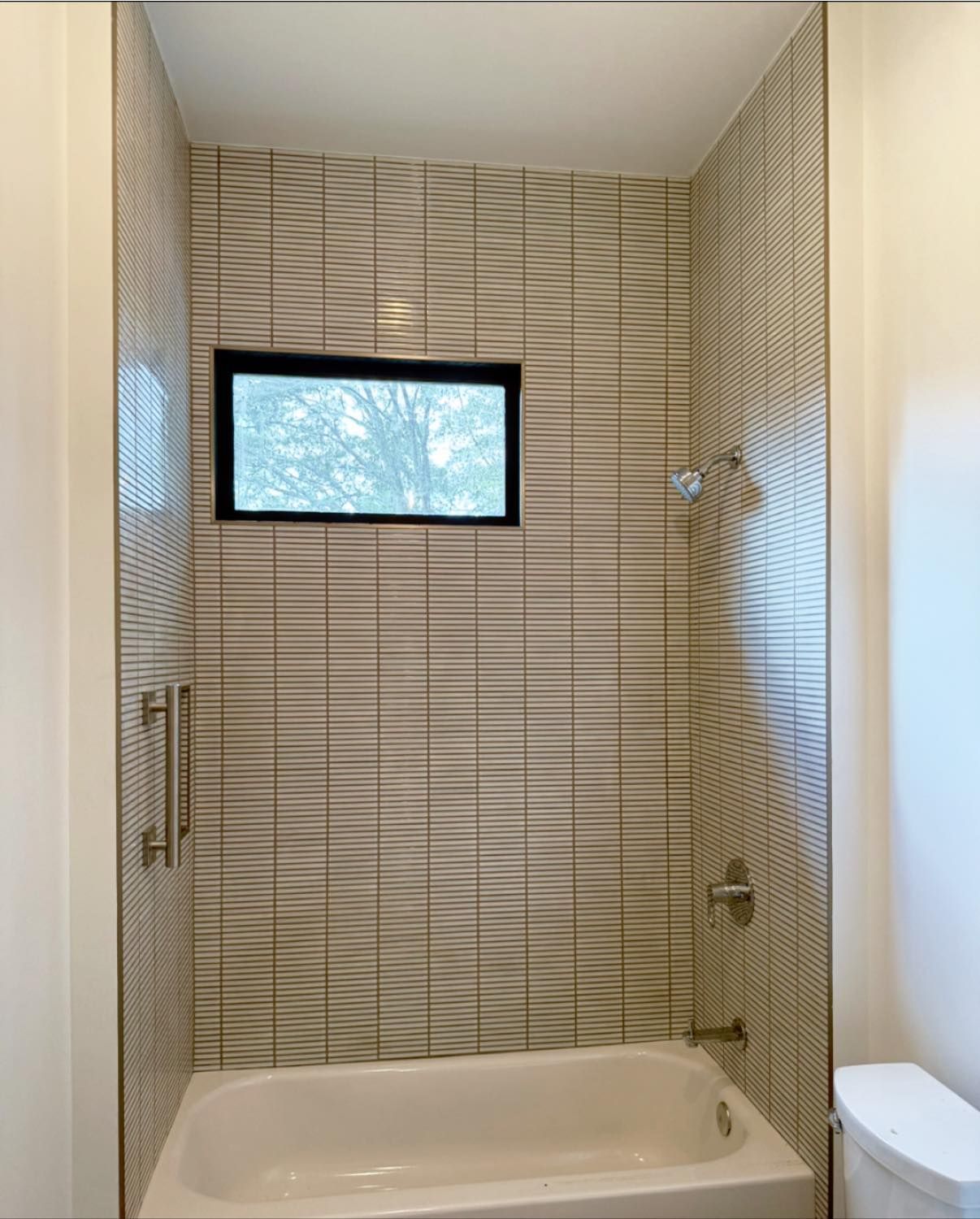 Bathroom with white tub, tiled shower walls, small window, and silver fixtures.
