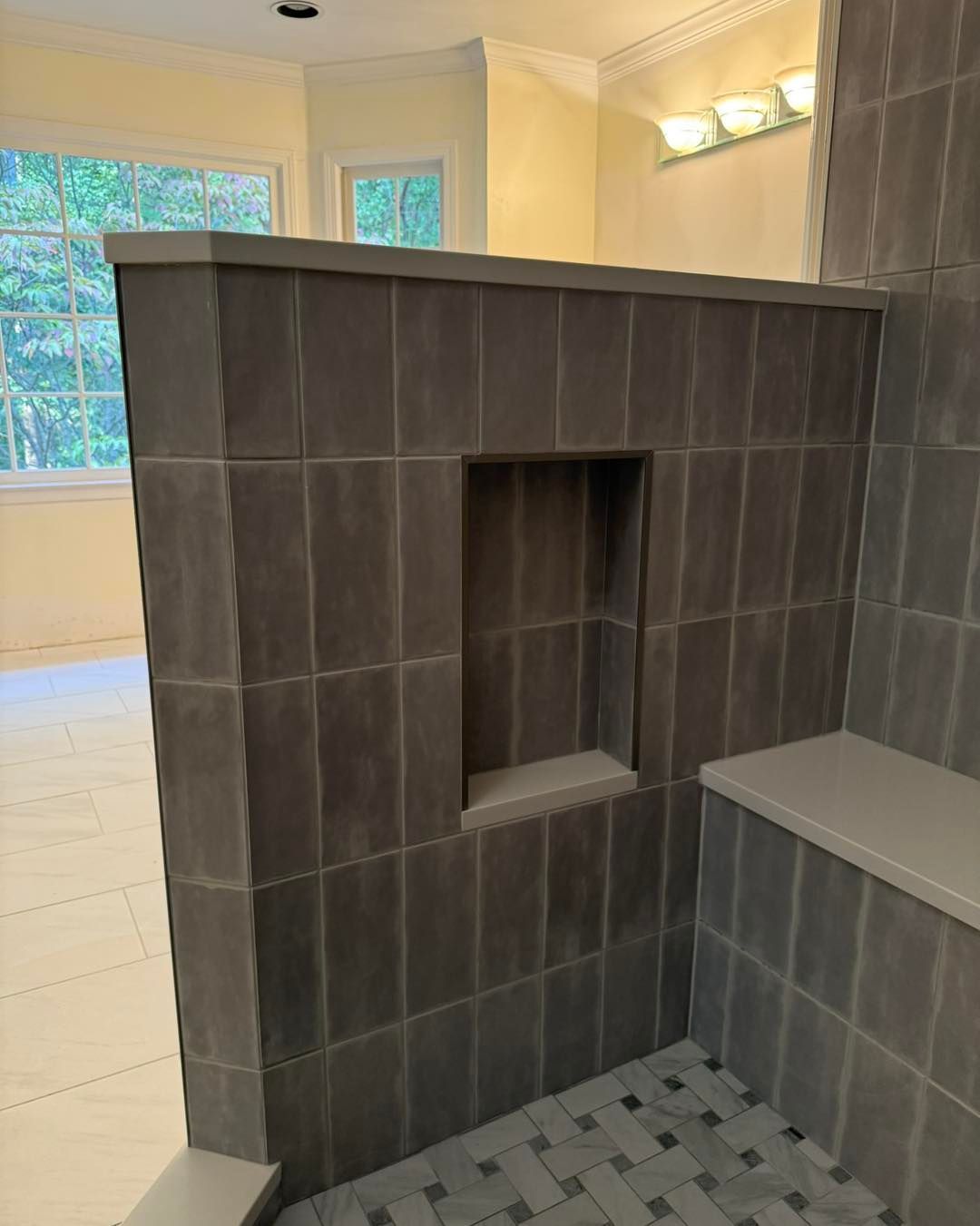 Gray tiled shower with a built-in shelf, bench, and mosaic floor.