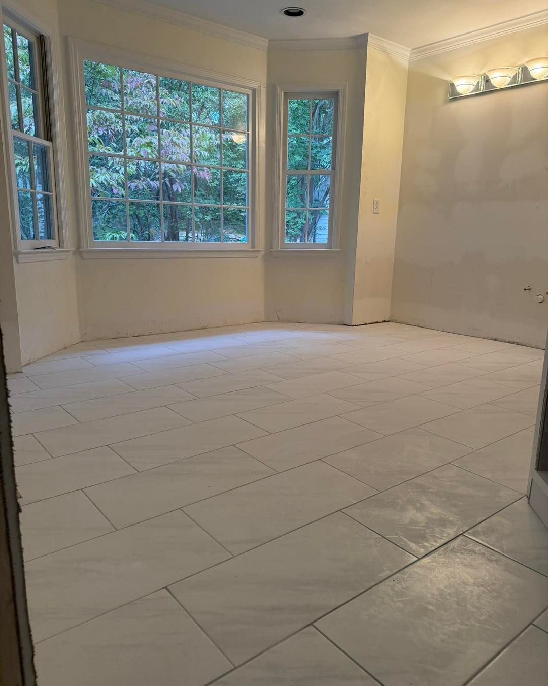 Spacious bathroom with white tile floor, large windows, and light walls; appears newly renovated.