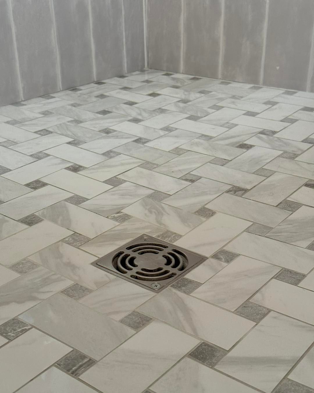 Shower floor with white and gray patterned tile; metal drain in center.