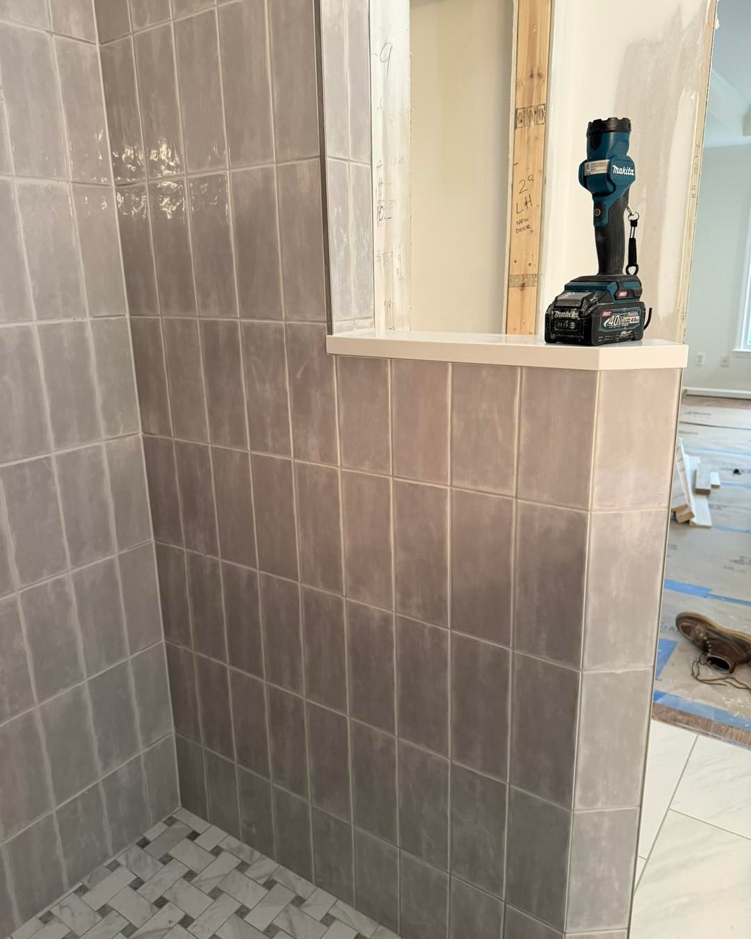Gray tiled shower enclosure under construction, with a cordless drill on a shelf.