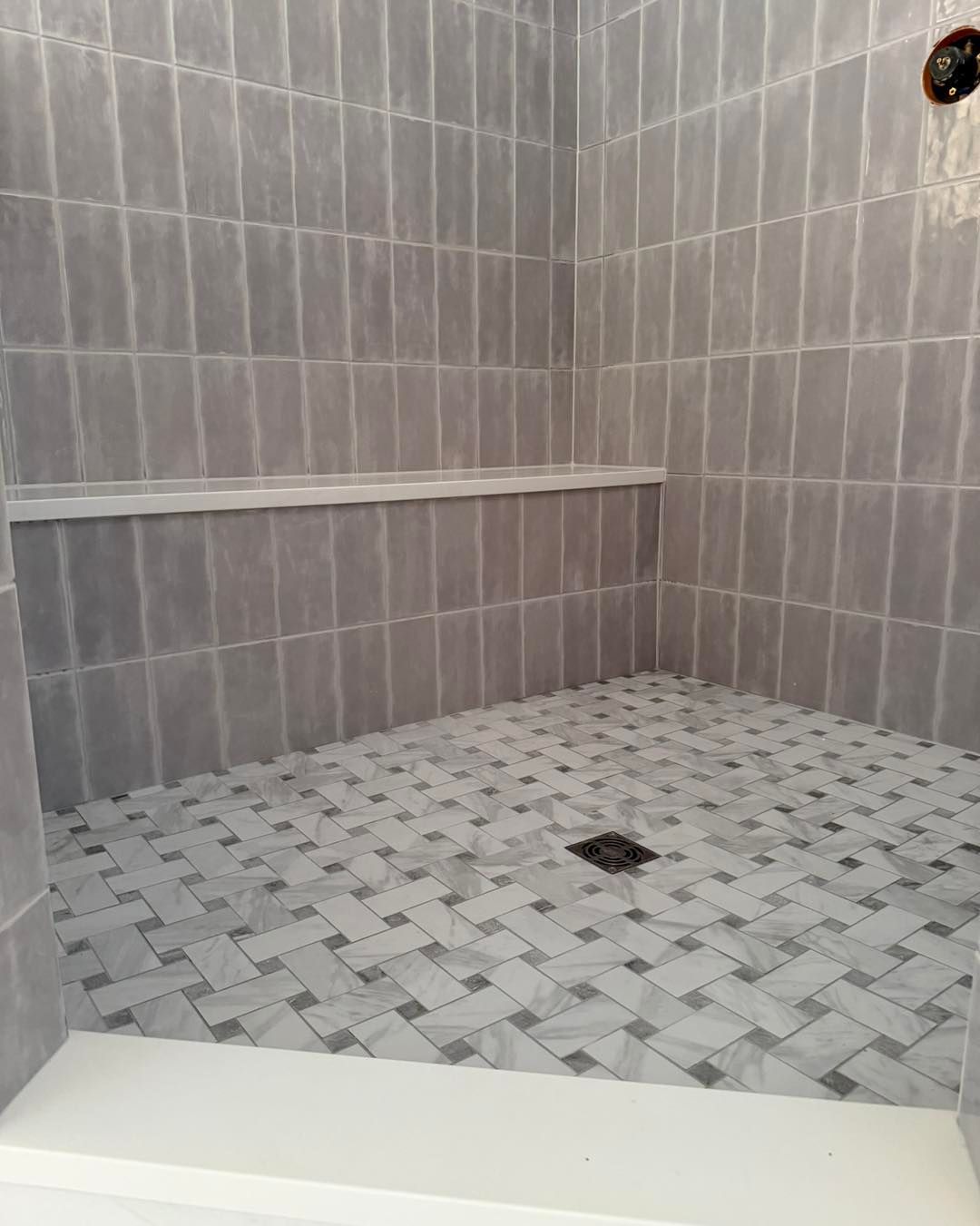 Gray tiled shower with herringbone floor pattern and built-in shelf.