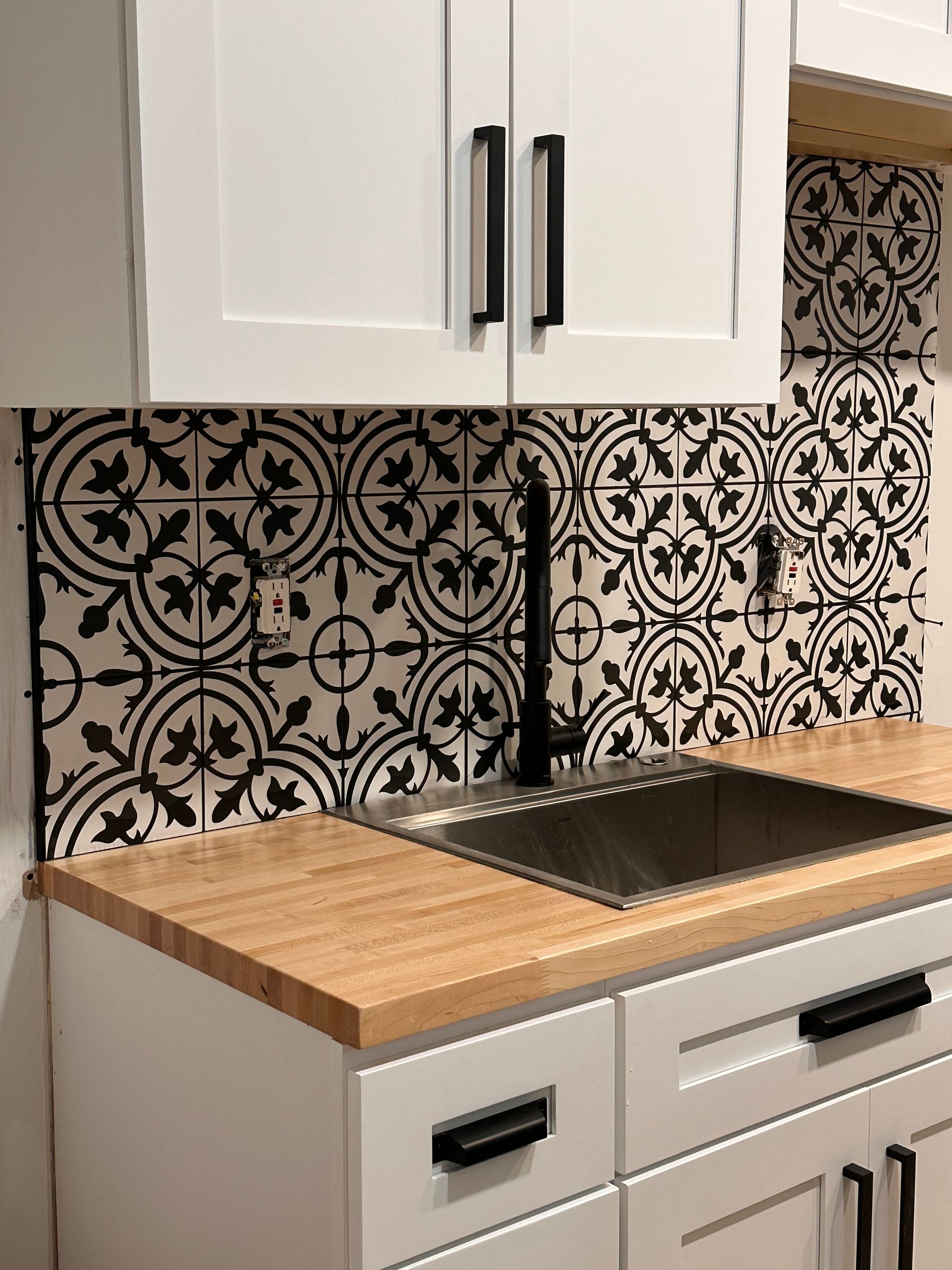 Modern kitchen with white countertops, gray and white patterned backsplash, and dark wood cabinets.