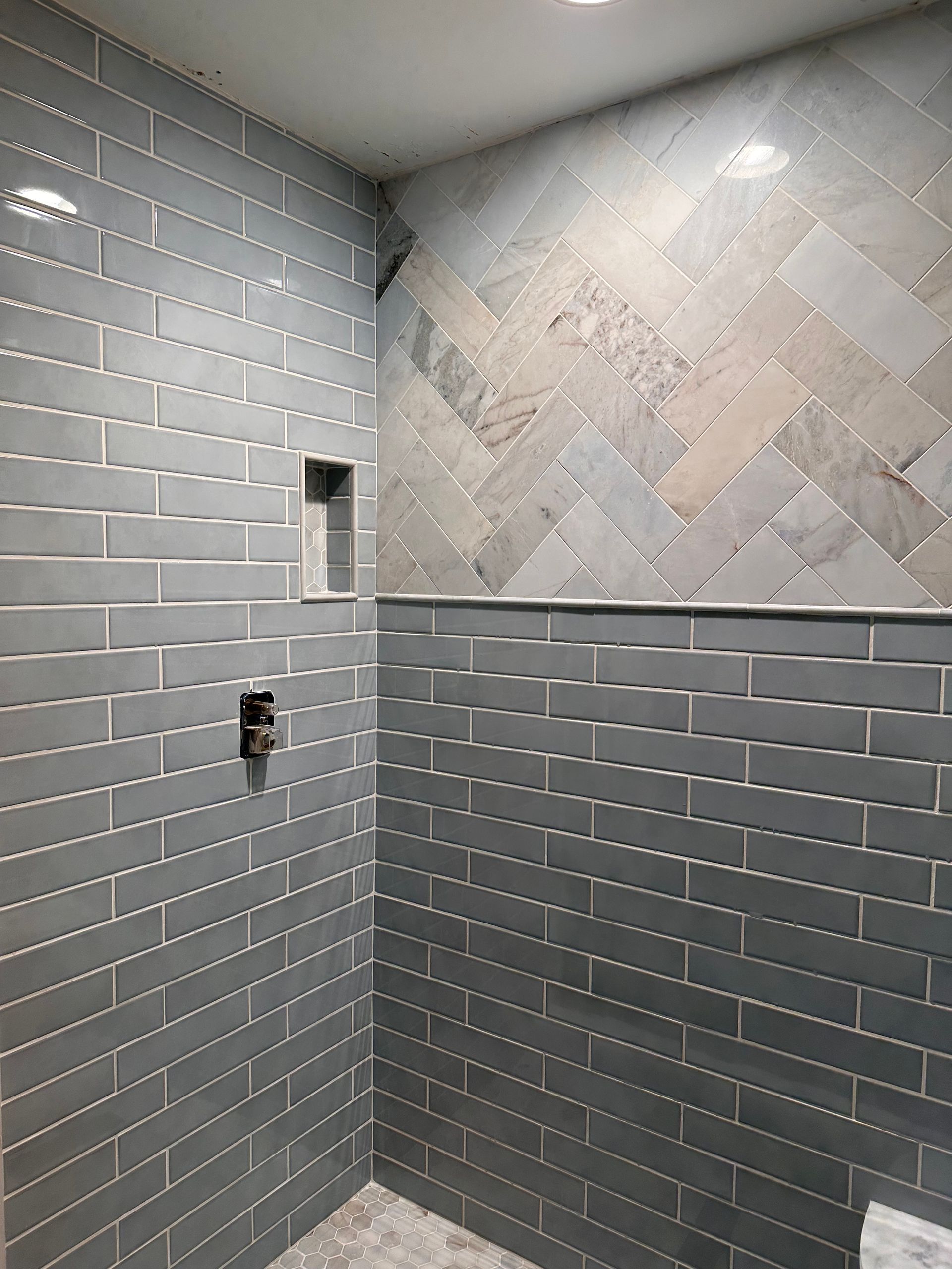 Marble shower with decorative tile niche and glass door.