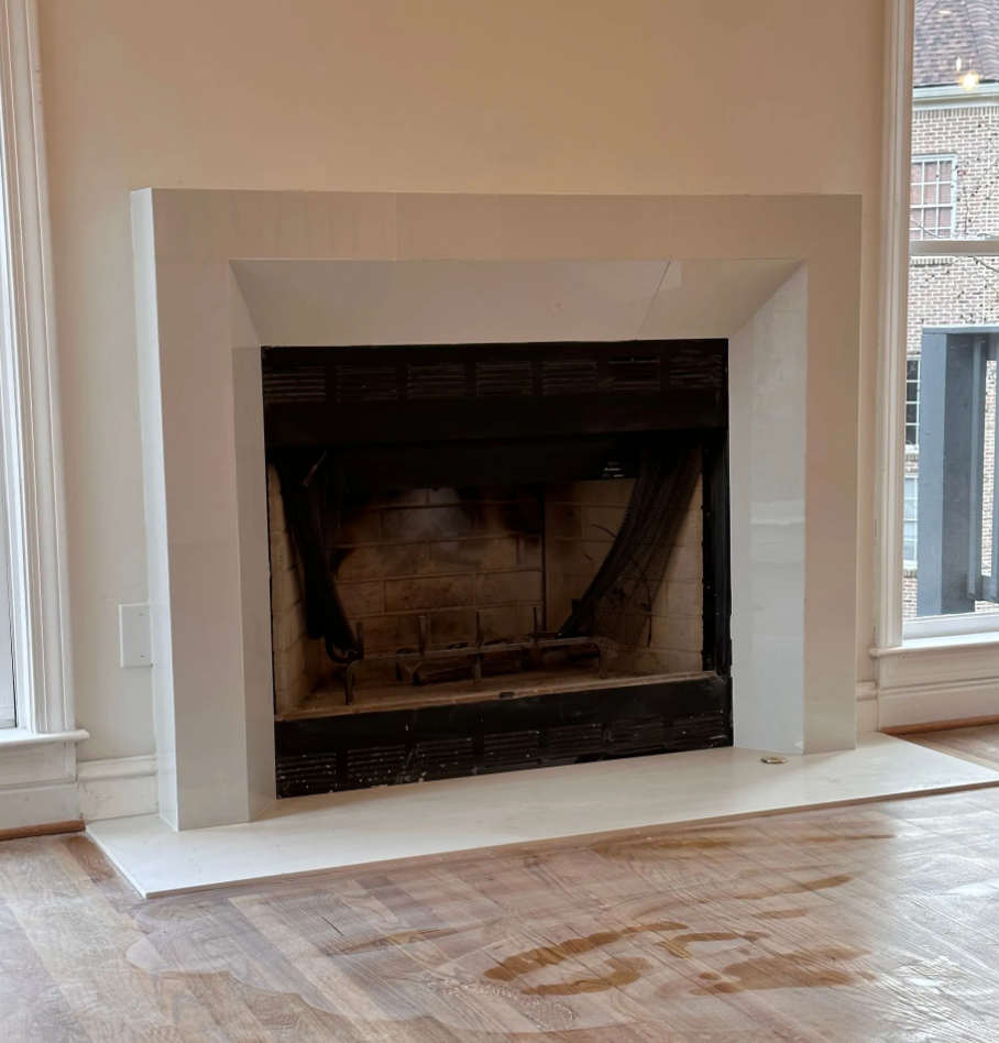 Modern fireplace with burning flames, black frame, and glass front. Gray chair on left.