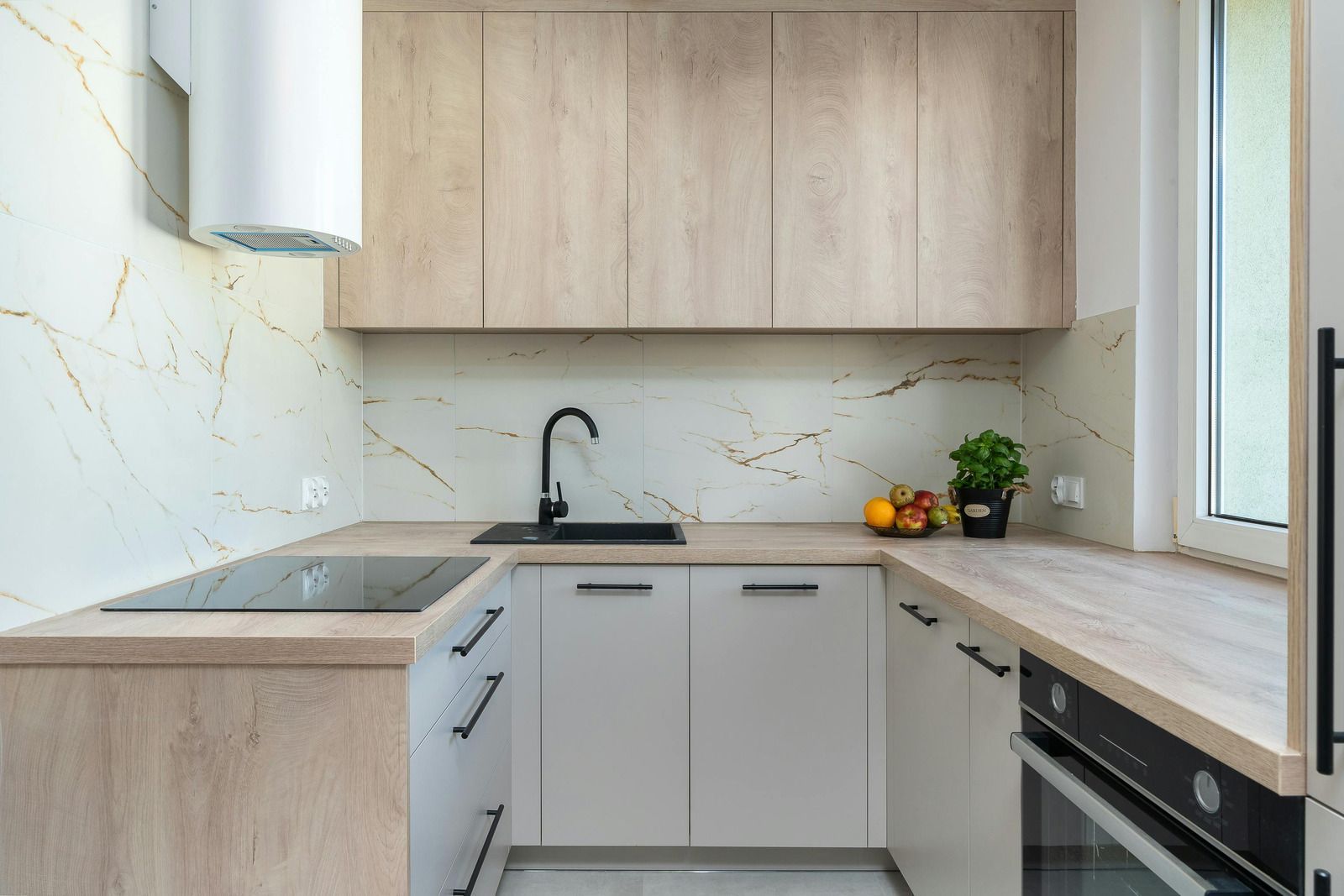 U-shaped modern kitchen with light wood cabinets, white countertops, black fixtures, and a window.