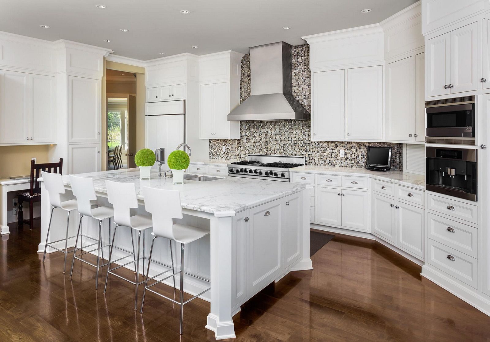 White kitchen with island and seating, stainless steel appliances, dark wood floors.